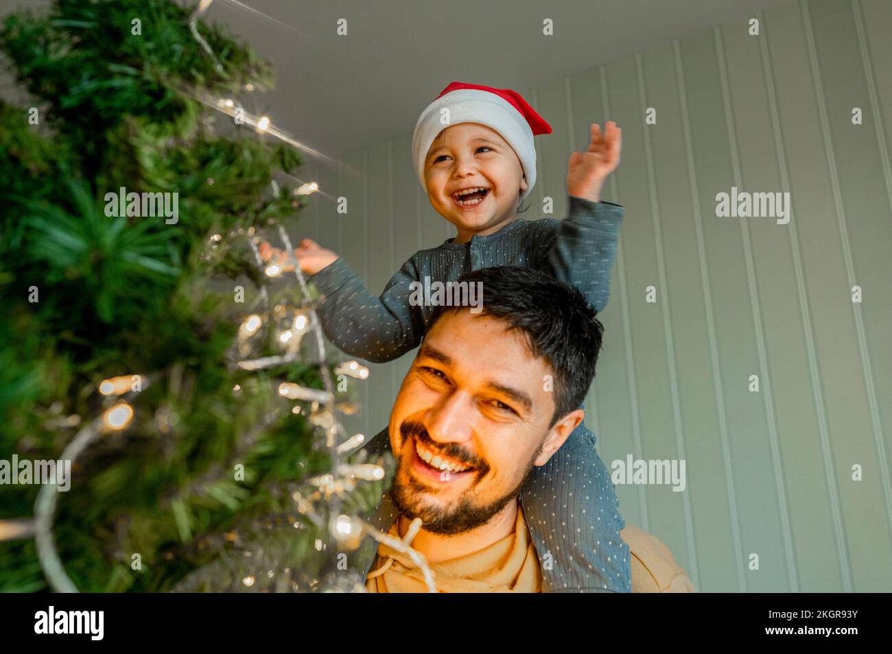 Sorridente ragazzo seduto sulla spalla del padre che ha divertente decorare l'albero di Natale a casa Foto Stock