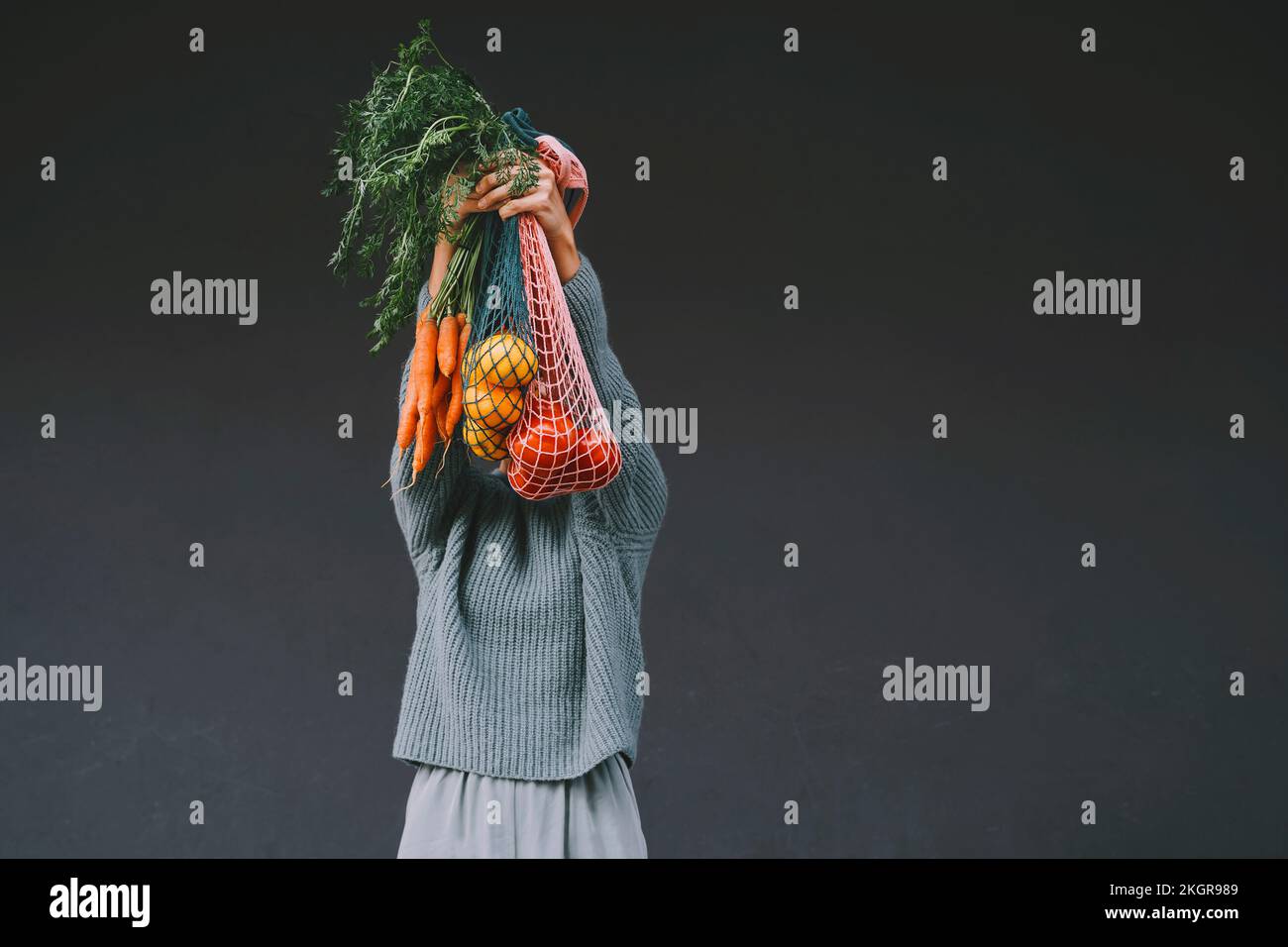 Donna che copre il viso con carote e frutta in sacchi a rete Foto Stock