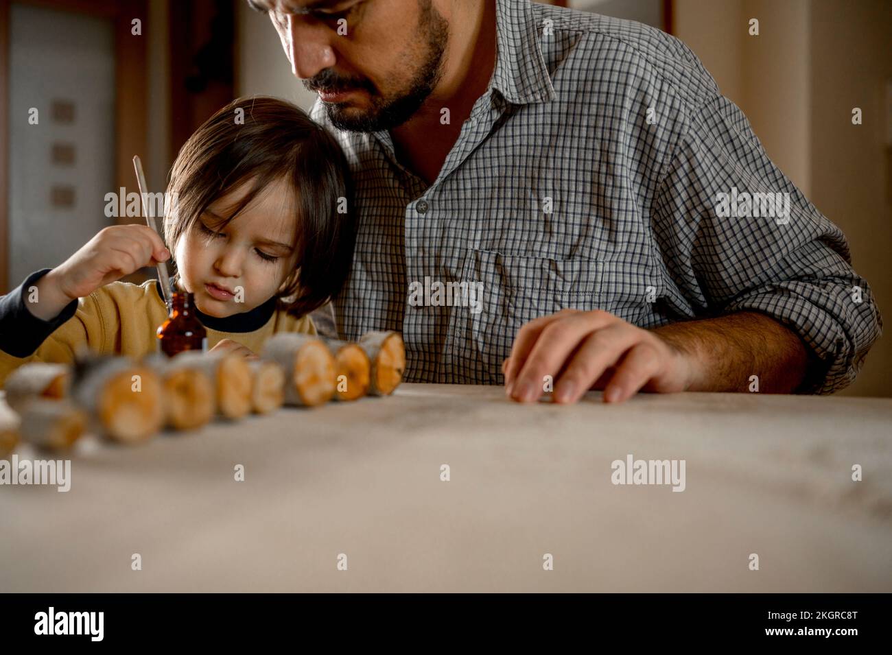 Padre che assiste figlio spazzolando olio su legno Foto Stock