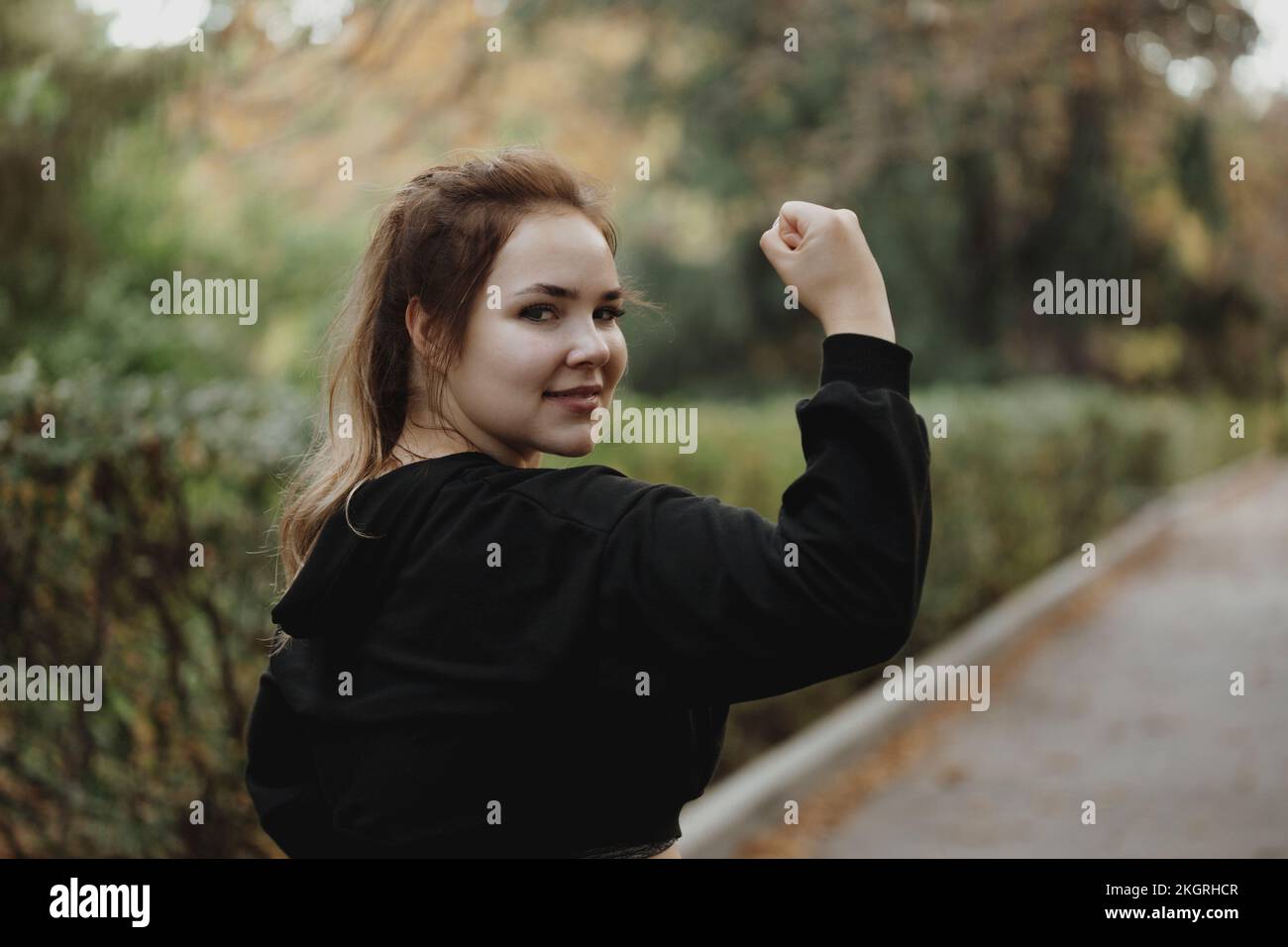Giovane donna sorridente che flette i muscoli nel parco Foto Stock Giovane donna sorridente che flette i muscoli nel parco Foto Stock