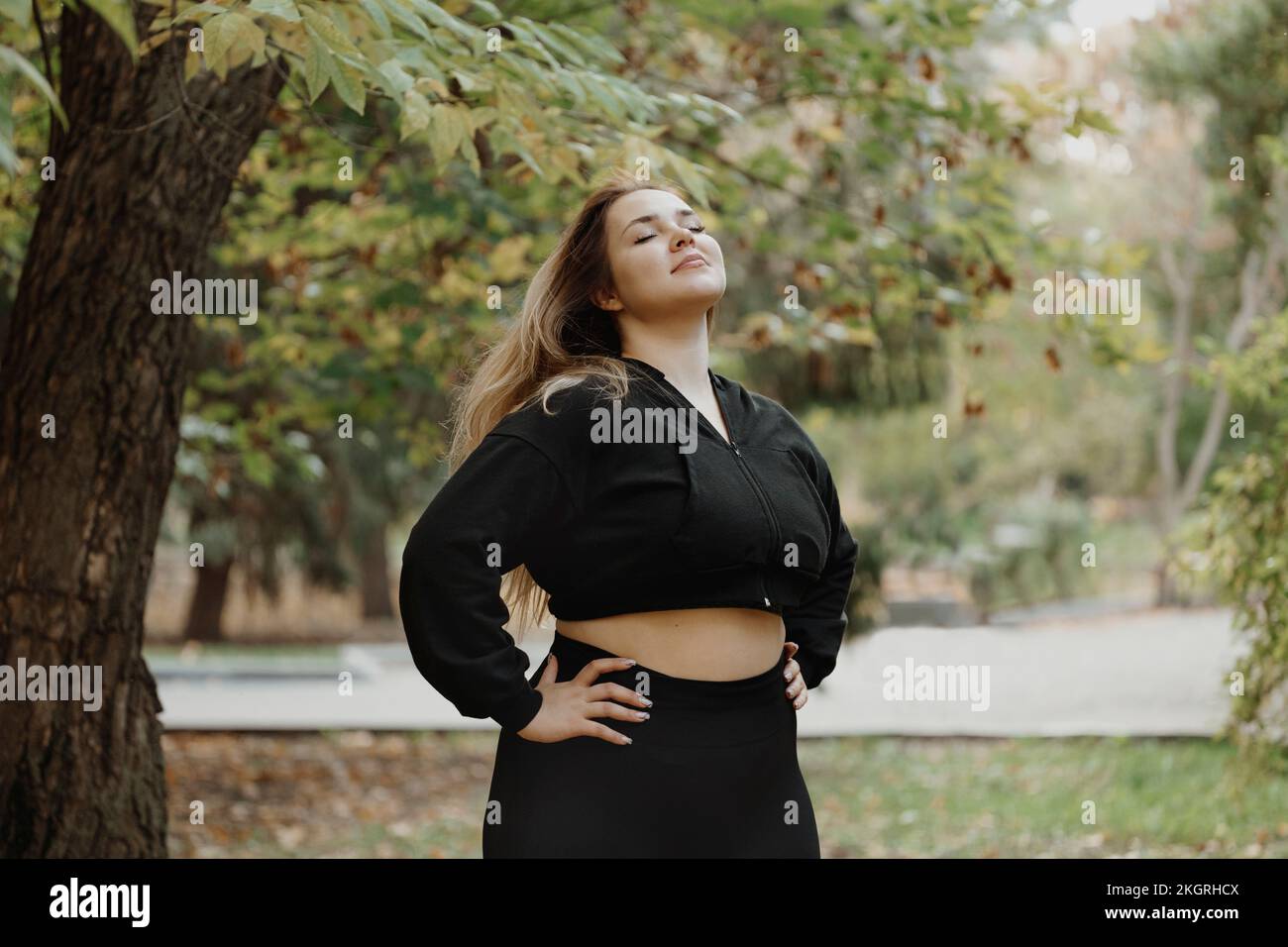 Giovane donna sorridente in piedi con le mani sui fianchi che respirano aria fresca al parco Foto Stock