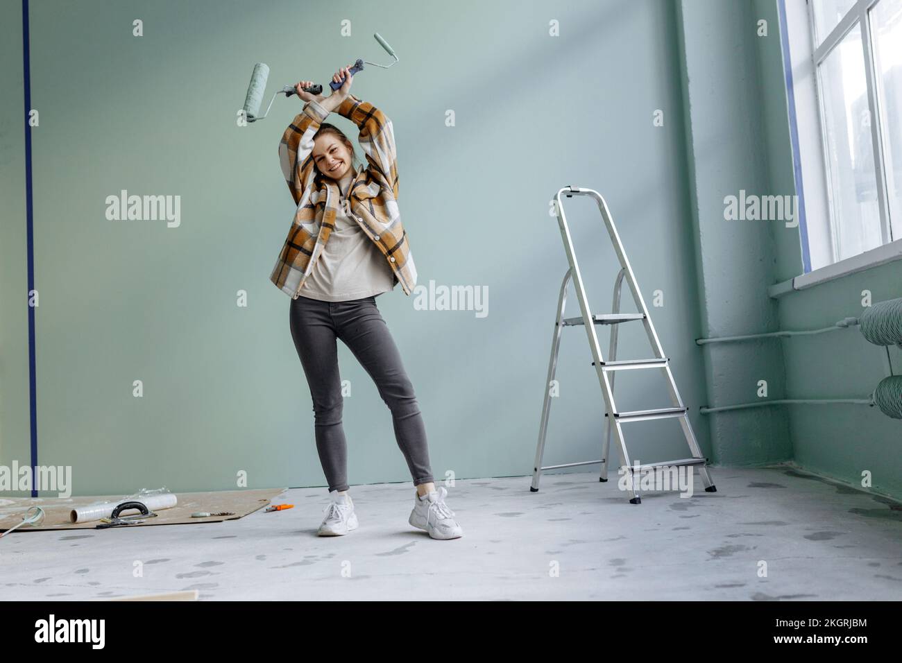 Giovane donna sorridente che balla con gli attrezzi di lavoro a casa Foto Stock