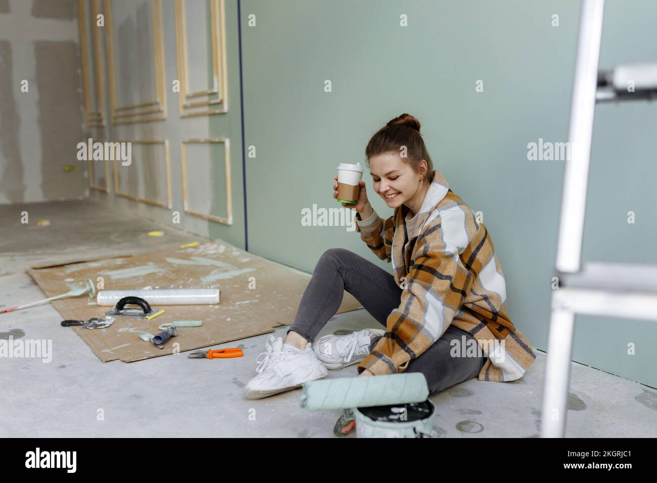 Donna sorridente con rullo di vernice che ha il caffè in appartamento disordinato Foto Stock