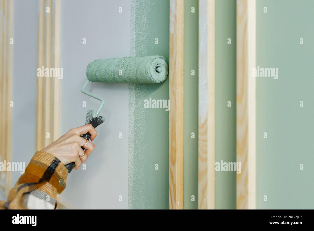 Giovane donna che dipinge con un rullo di pittura sul muro in appartamento Foto Stock