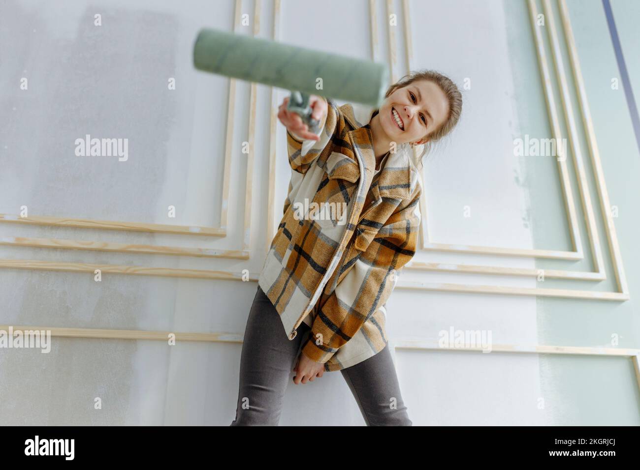 Donna sorridente con rullo di vernice di fronte al muro a casa Foto Stock