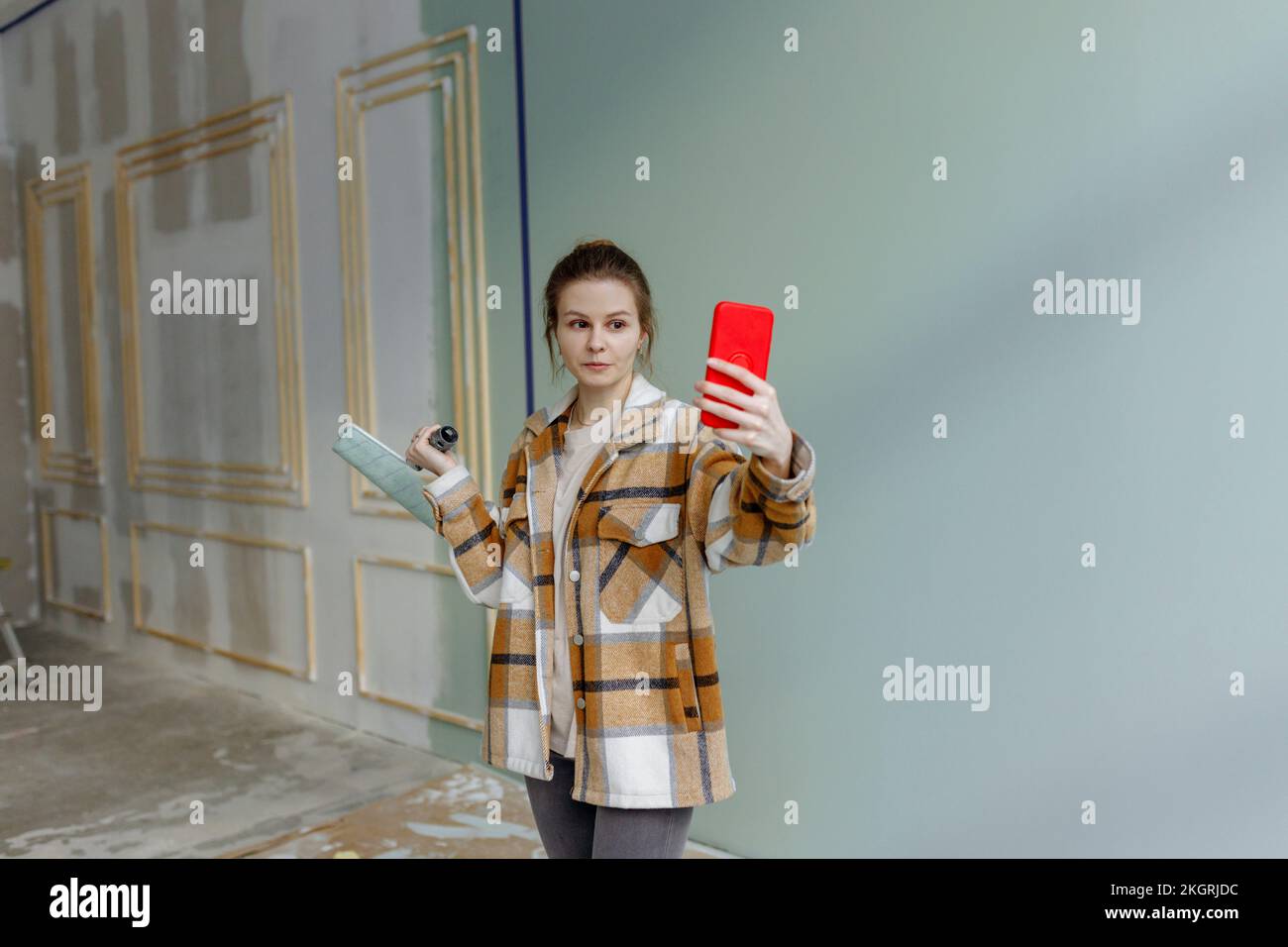 Giovane donna con rullo di vernice che porta selfie sullo smartphone a casa Foto Stock