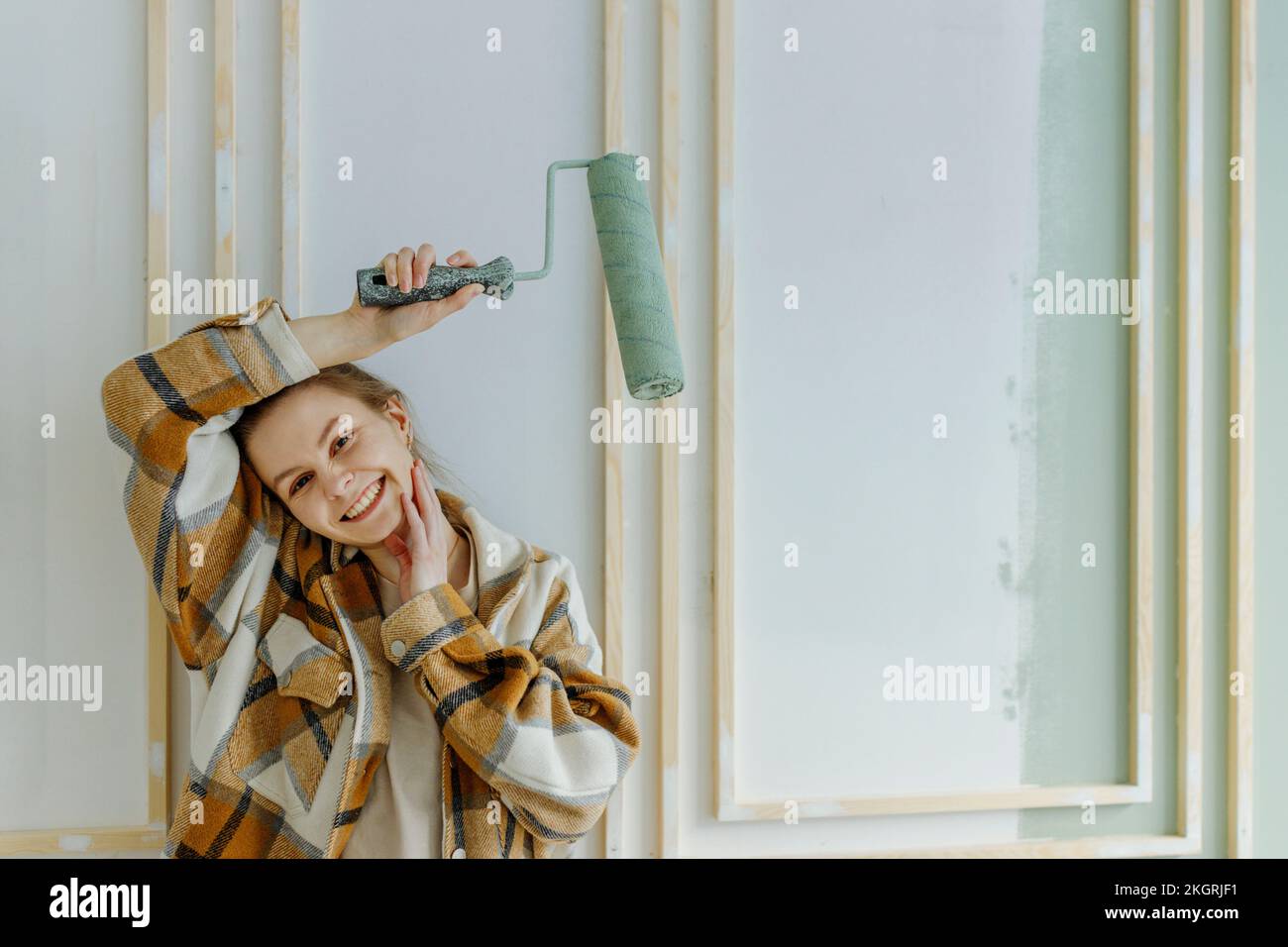 Giovane donna sorridente che tiene rullo di vernice sopra la testa a casa Foto Stock