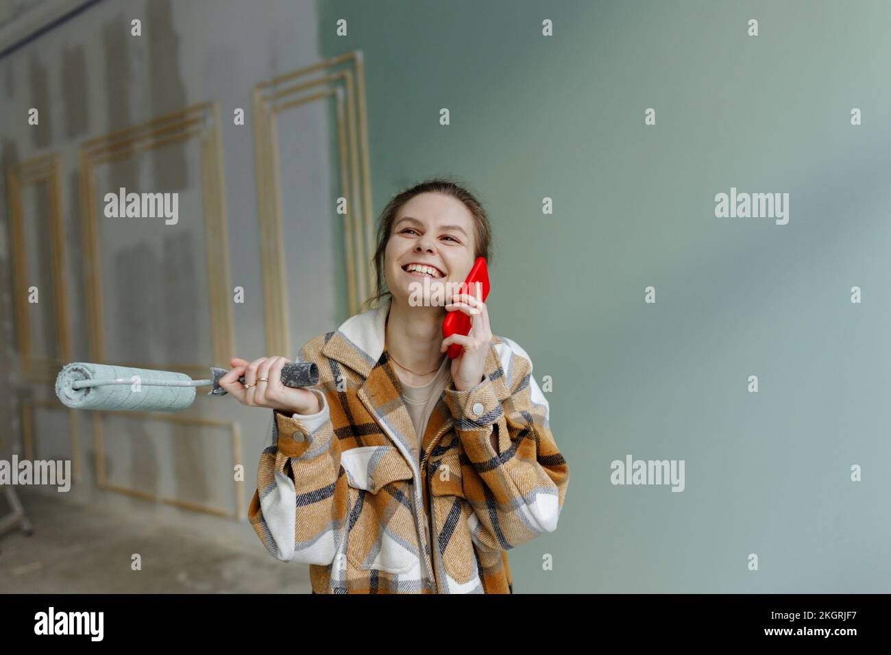 Donna felice con rullo di vernice che parla sullo smartphone in appartamento Foto Stock