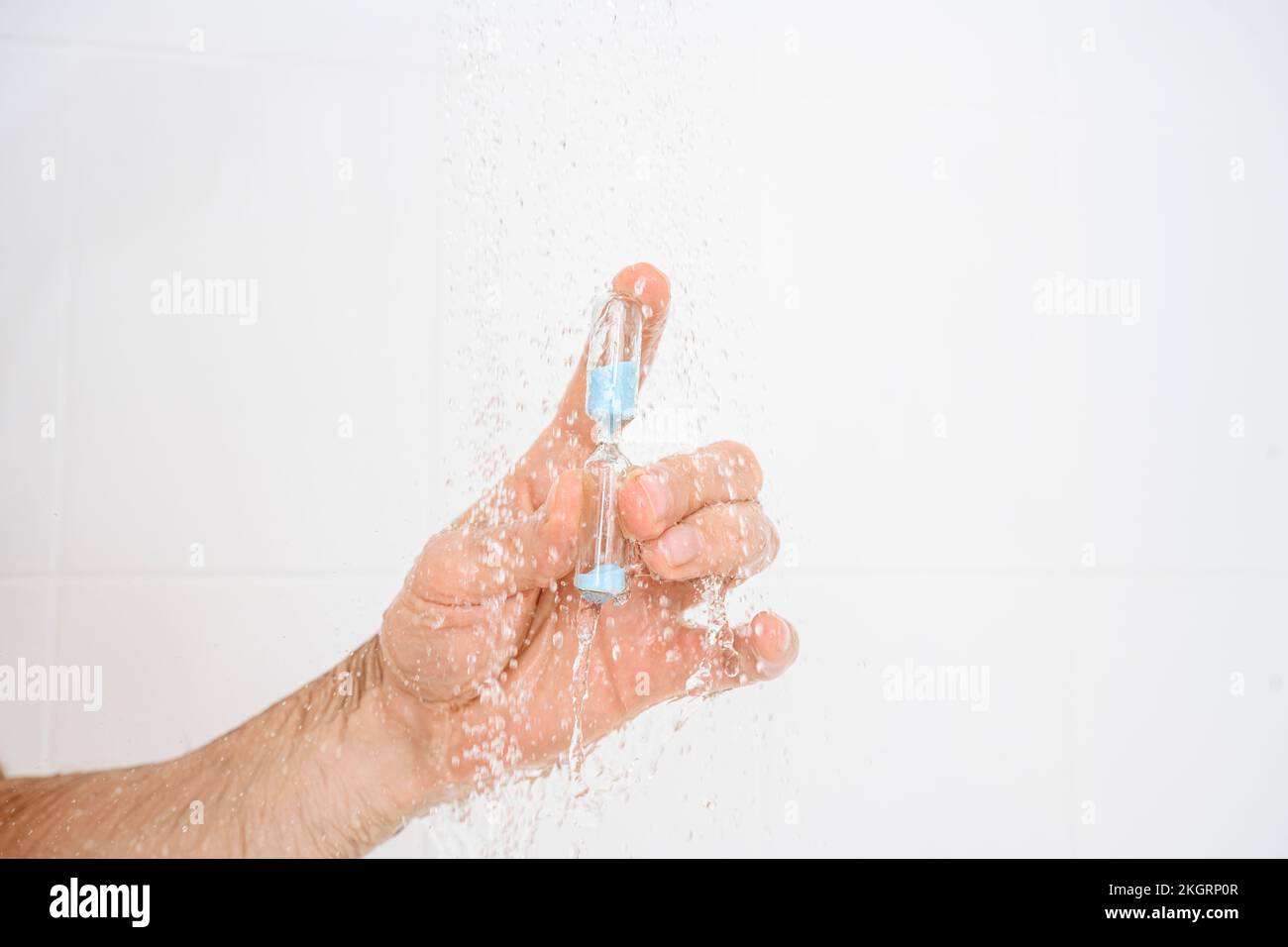 Mano dell'uomo che tiene la clessidra in acqua sotto la doccia Foto Stock