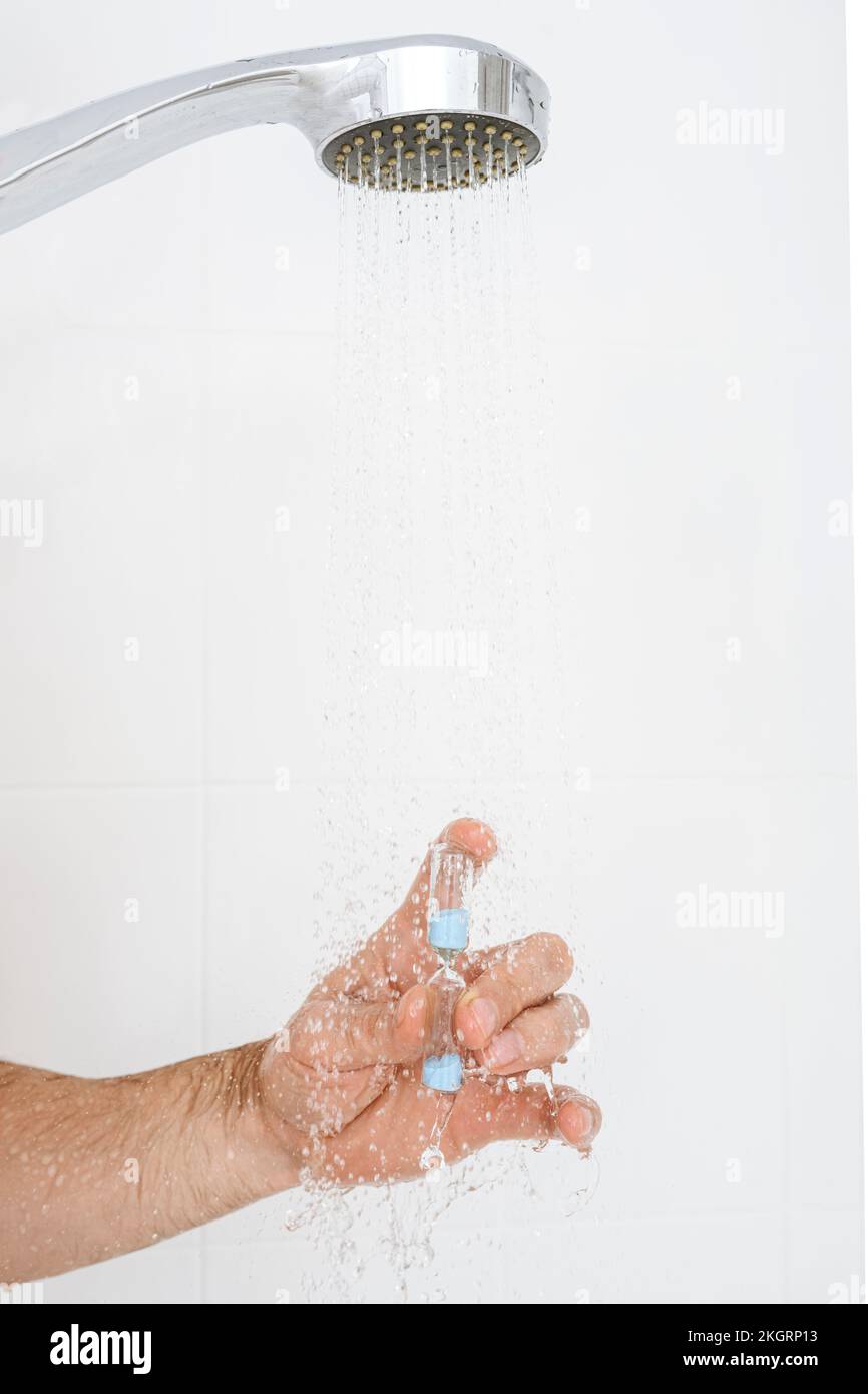 Mano dell'uomo che tiene la clessidra in acqua sotto la doccia a casa Foto Stock