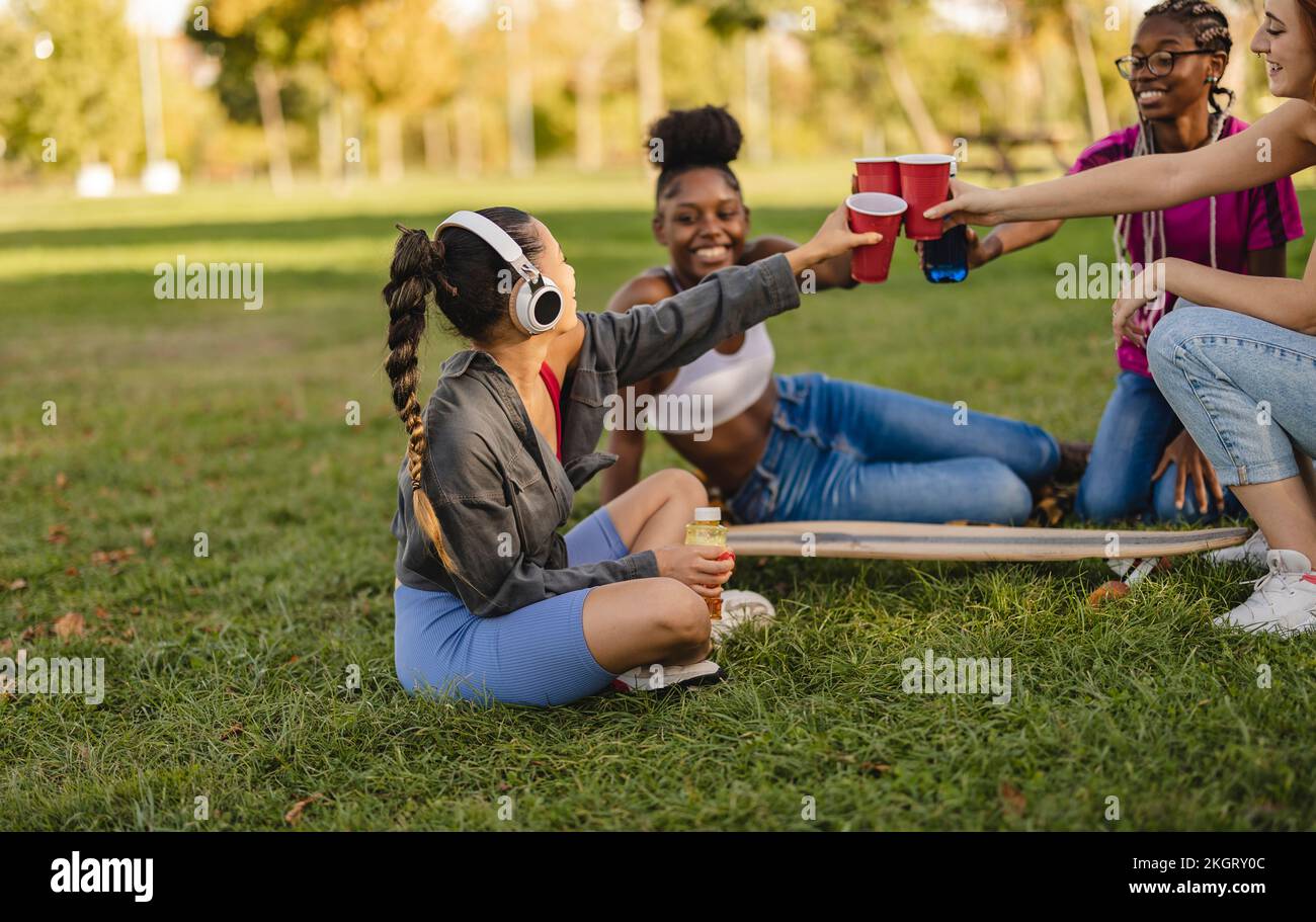 Giovani amici che brinda tazze usa e getta seduti al parco Foto Stock