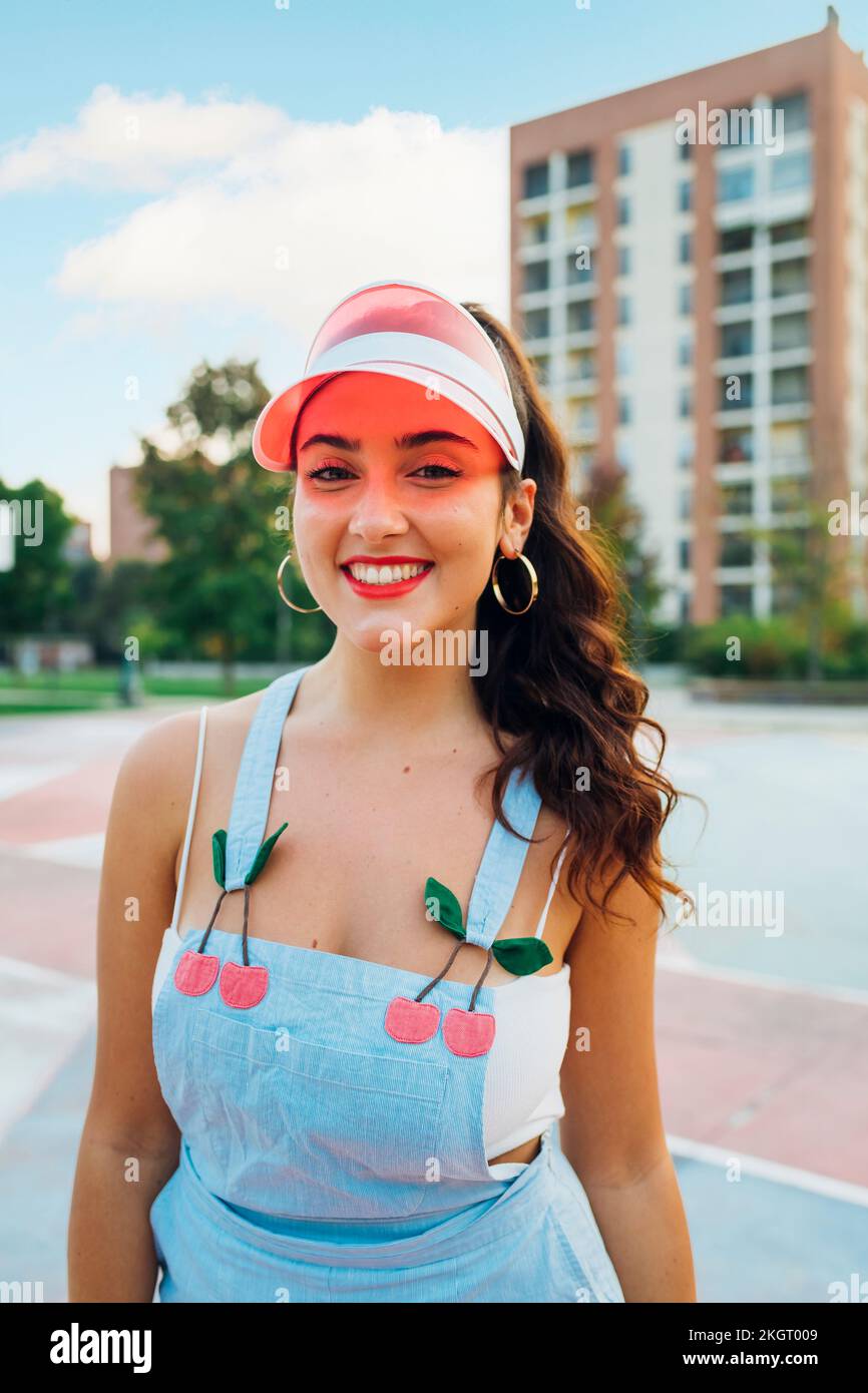 Giovane donna sorridente che indossa la visiera parasole a un campo sportivo Foto Stock