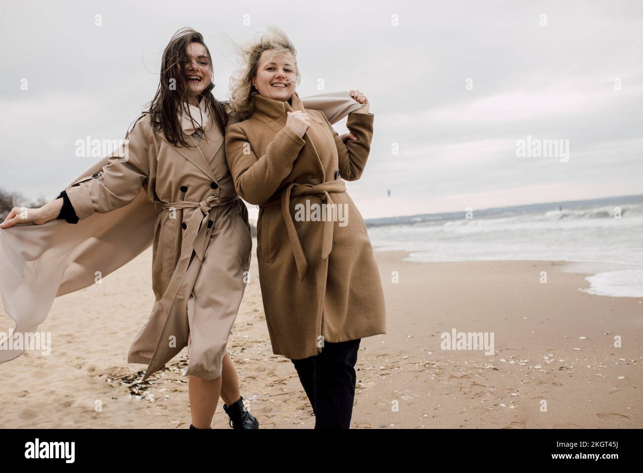 Madre e figlia indossano cappotti che si divertono in spiaggia Foto Stock
