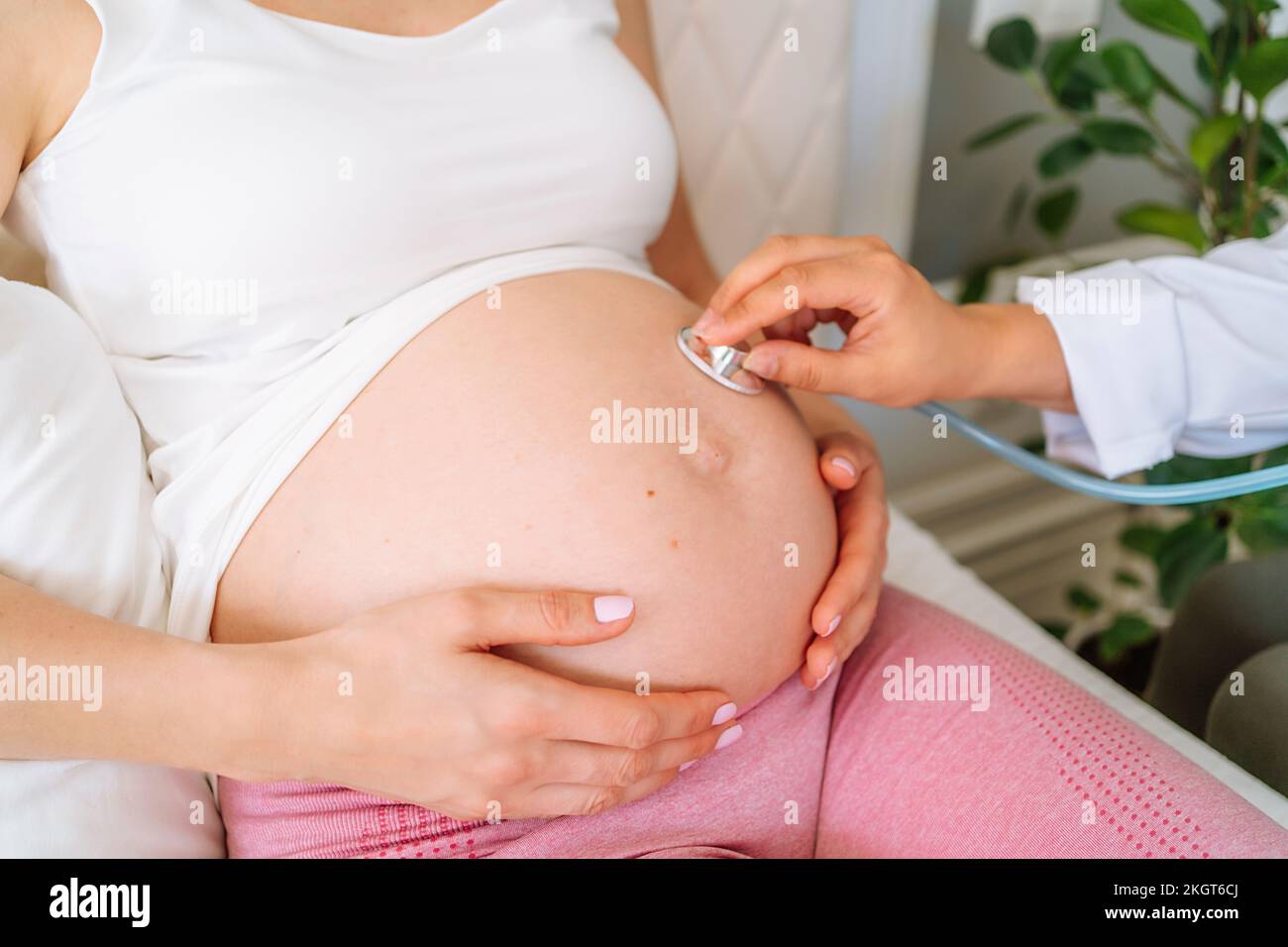 Medico con stetoscopio che esamina la donna incinta a casa Foto Stock