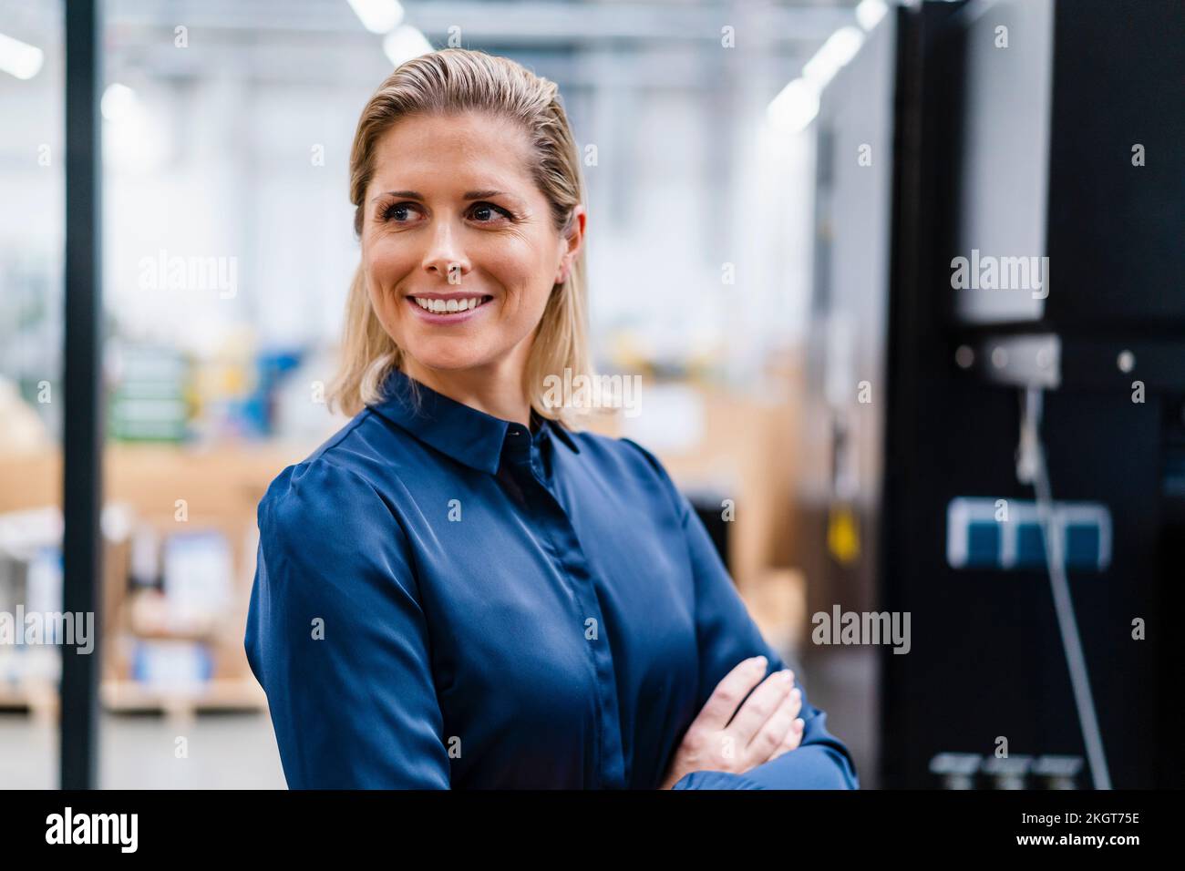 Donna d'affari sorridente che indossa una camicia blu in fabbrica Foto Stock