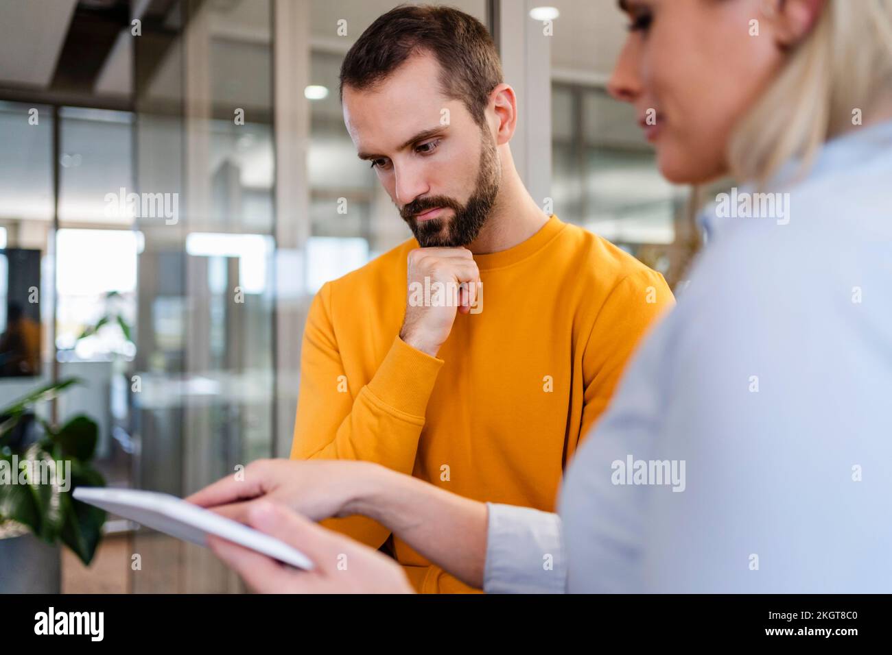 Uomo d'affari dedicato con la mano sul mento che guarda il tablet PC tenuto da un collega Foto Stock