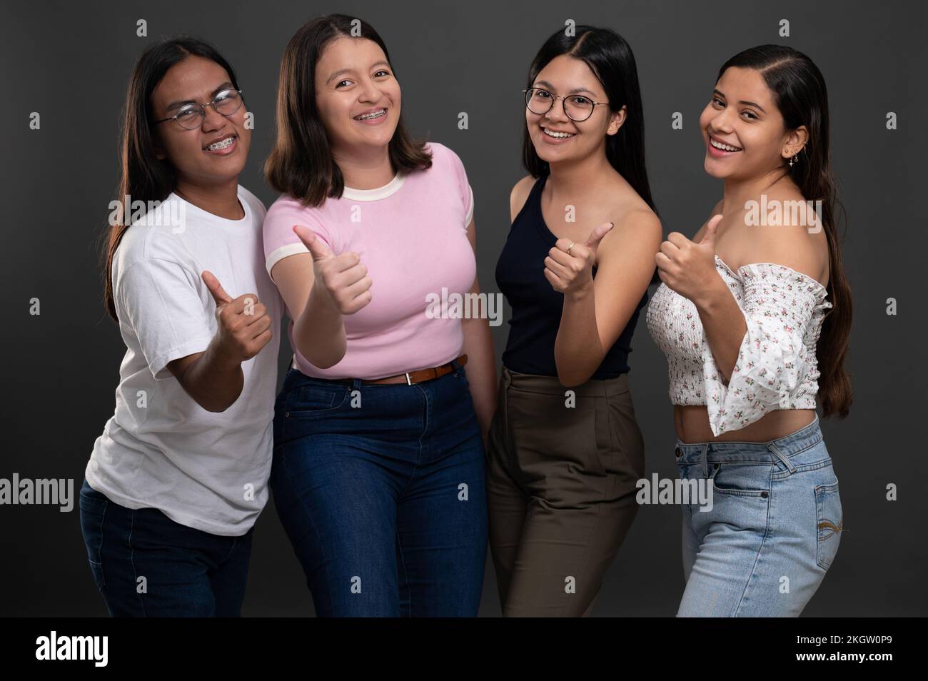 Gruppo di giovani ispanici con pollice in su sul backgroind grigio studio con sorriso amichevole Foto Stock