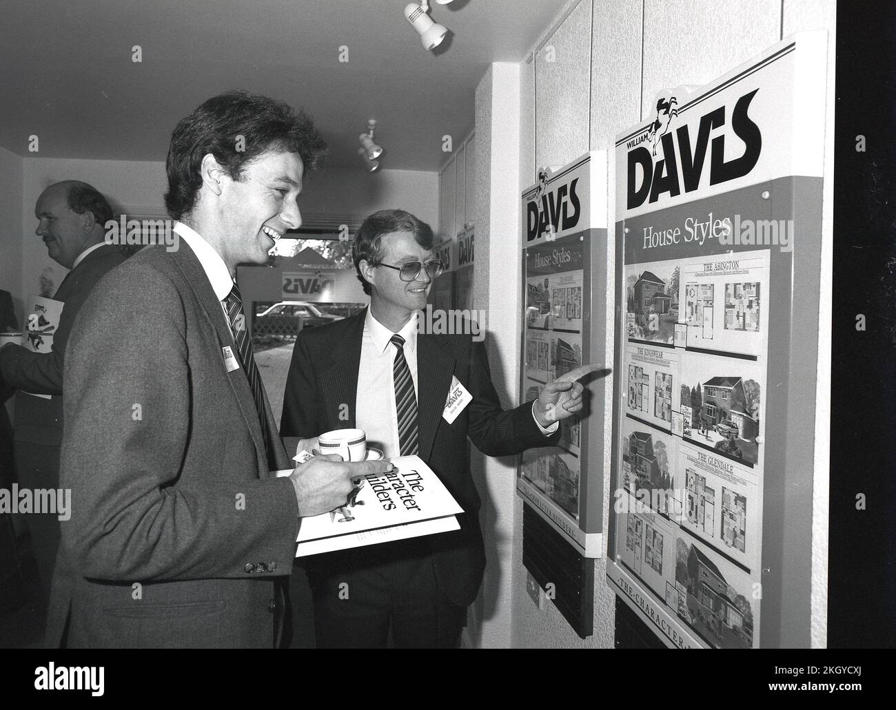 1986, storico, un giornalista in possesso di una tazza di caffè e di un opuscolo aziendale che viene mostrato da un venditore immagini dei diversi stili di casa disponibili in un nuovo sviluppo di alloggi, Sheppshed, Leicestershire, Inghilterra, Regno Unito. Foto Stock