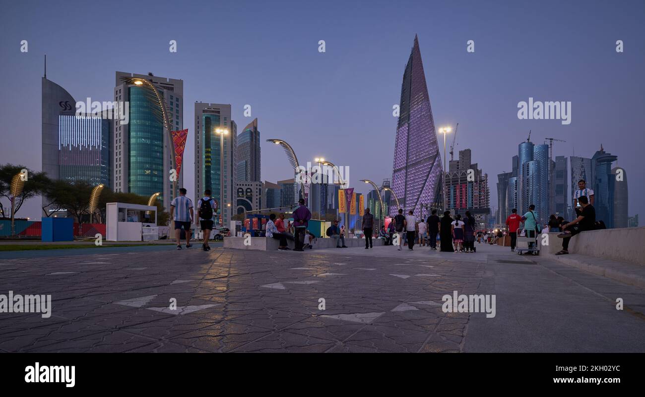 Foto al tramonto sulla Corniche di Doha che mostra la preparazione del Qatar per la Coppa del mondo FIFA Qatar 2022 con gente del posto e visitatori che camminano sul lungomare Foto Stock