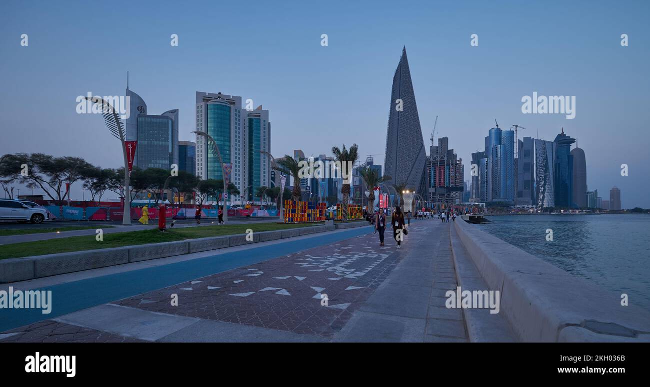 Foto al tramonto sulla Corniche di Doha che mostra la preparazione del Qatar per la Coppa del mondo FIFA Qatar 2022 con gente del posto e visitatori che camminano sul lungomare Foto Stock