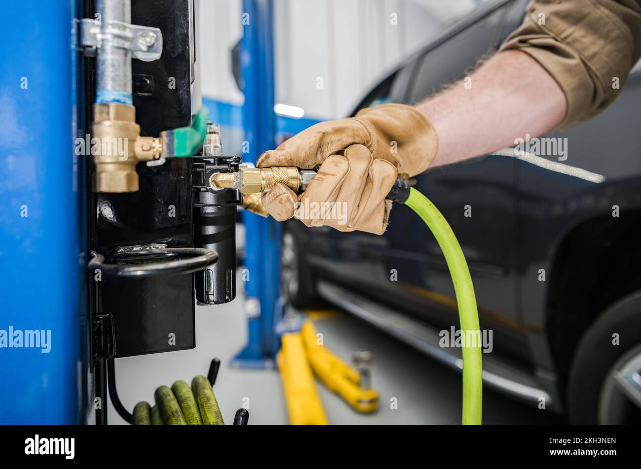 Primo piano di un meccanico collegamento di un tubo su un attrezzo compressore d'aria di ruota fisso installato in officina di automobile professionale. Foto Stock