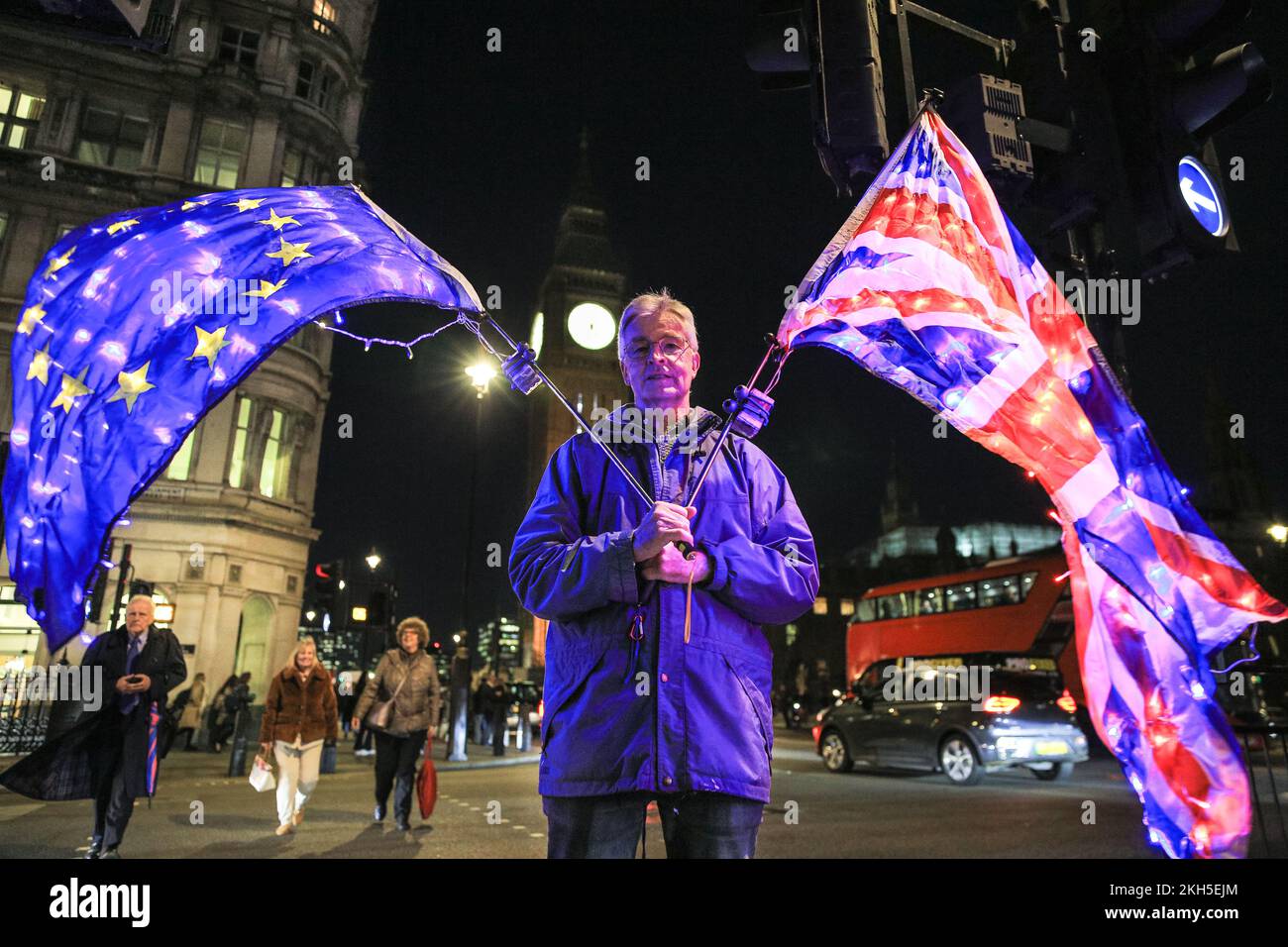 Westminster, Londra, Regno Unito. 23rd Nov 2022. Peter, un attivista con Sodem (Stand of Defiance European Movement), un gruppo di protesta intorno a Steve Bray, 'Westminster Stop Brexit Man', si trova su un'isola trafficata vicino alle Houses of Parliament con due bandiere illuminate, una bandiera britannica Union Jack e la bandiera blu dell'UE con le sue stelle gialle. Il gruppo di attivisti protesta regolarmente nella capitale contro la Brexit, per gli stretti legami con l’Europa e contro l’attuale governo. Credit: Imageplotter/Alamy Live News Foto Stock