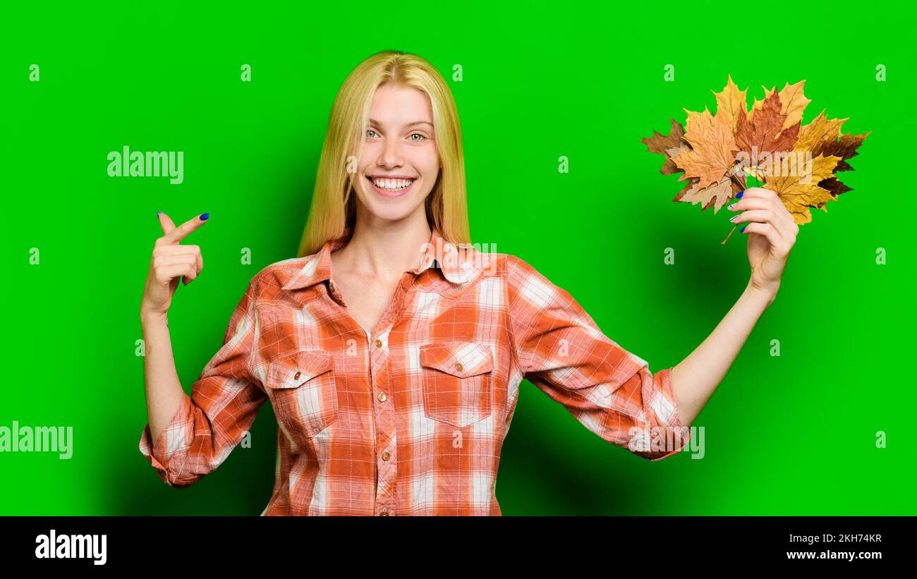 Donna sorridente che indica le foglie di acero in mano. Ragazza alla moda in camicia a quadri. Vendite autunnali. Foto Stock