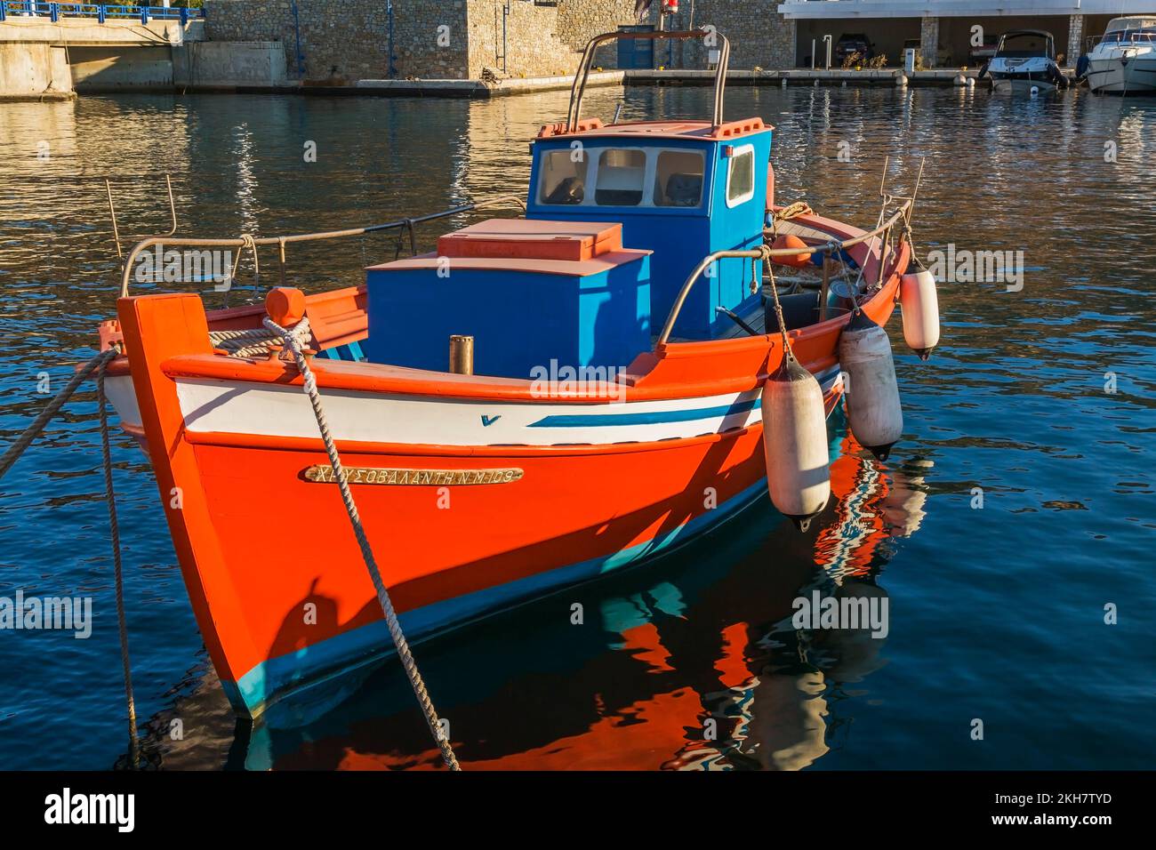 Piccola barca da pesca greca tradizionale arancione, bianca e blu con parabordi ancorata nel nuovo porto di Mykonos all'alba, isola di Mykonos, Grecia. Foto Stock