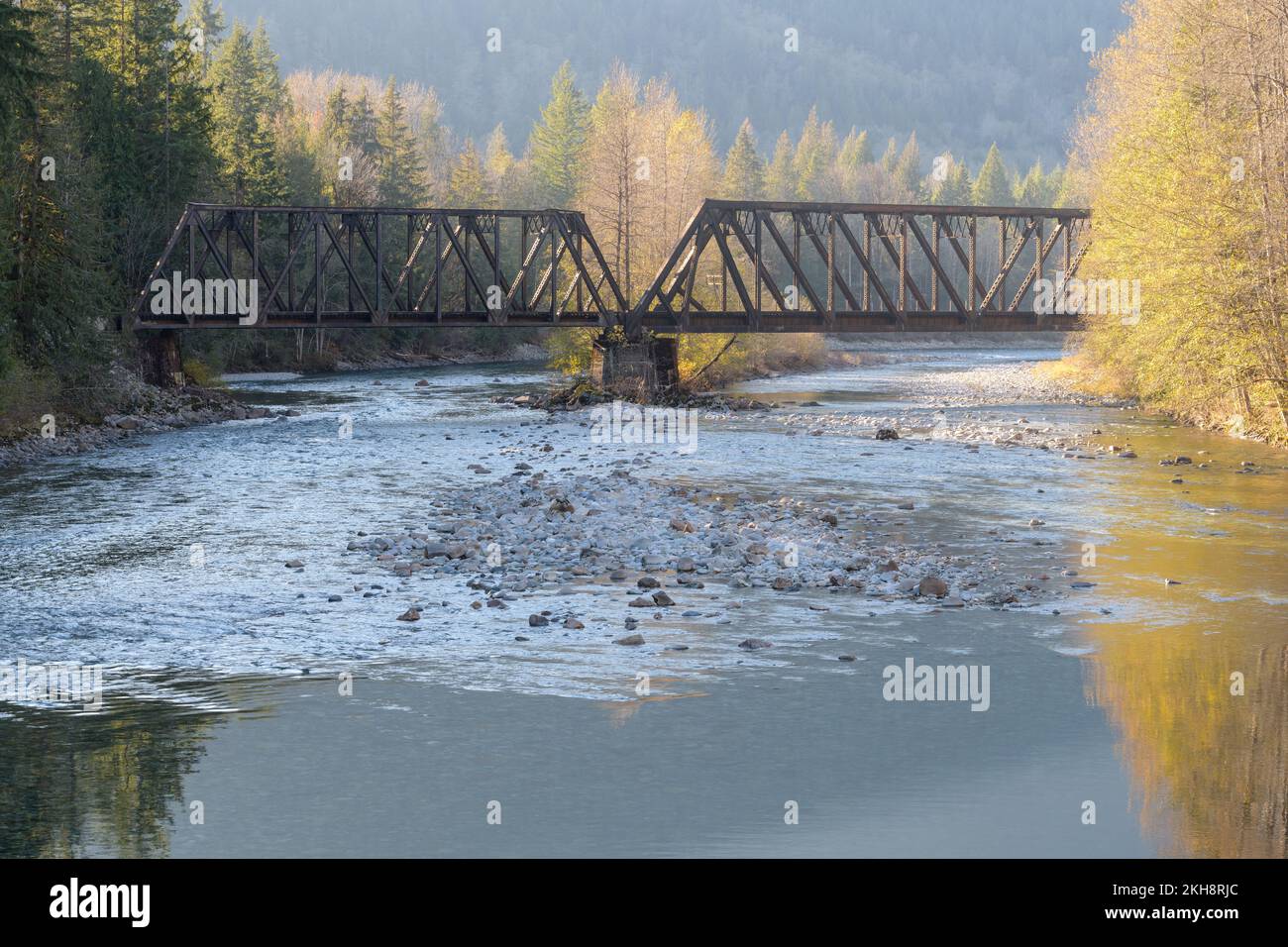 Il South Fork Skykomish River passa sotto un ponte ferroviario di metallo in tarda caduta con rocce fluviali visibili nell'acqua bassa Foto Stock
