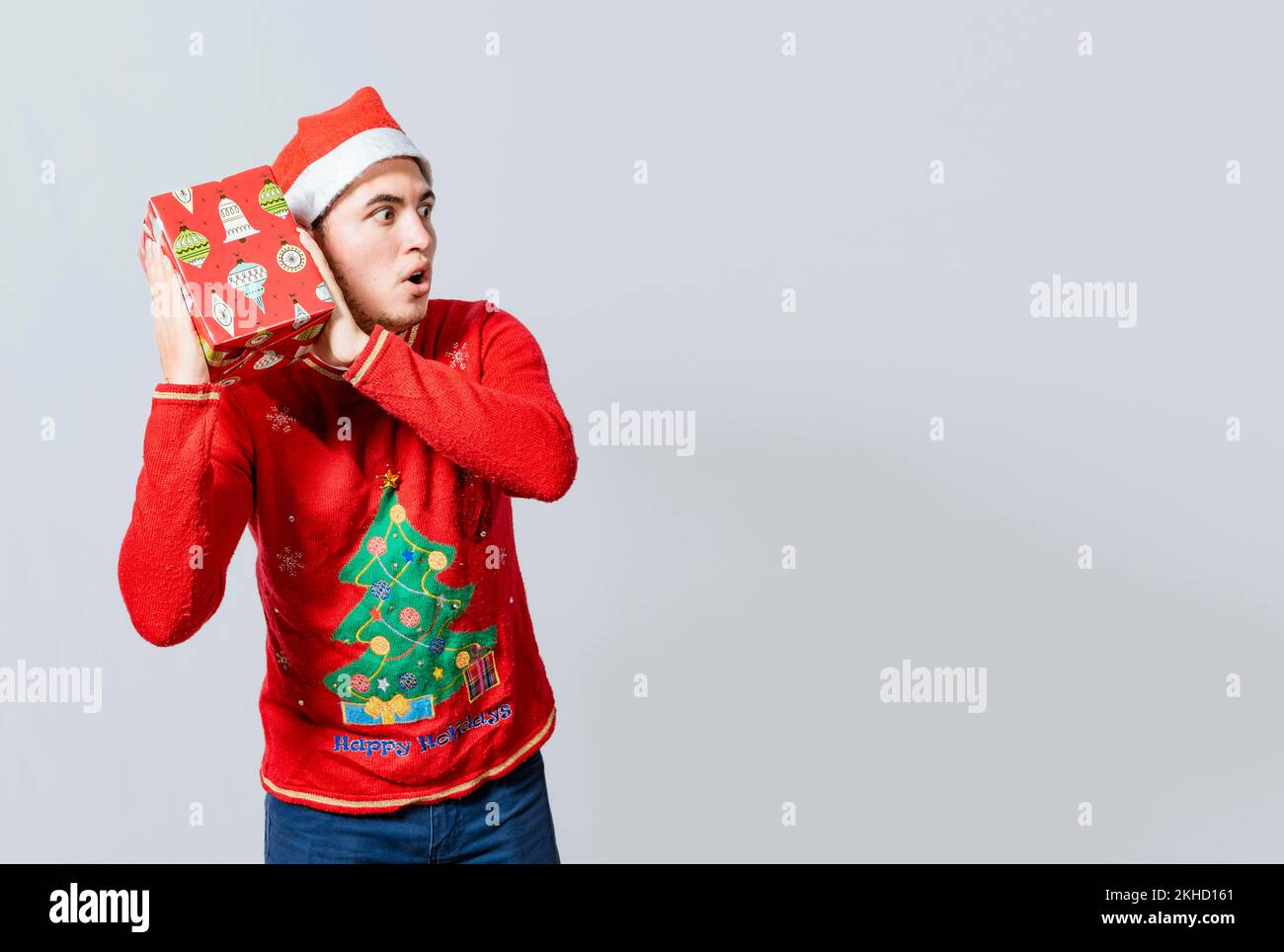 Ragazzo di Natale che tiene e ascolta una confezione regalo. Entusiasta gente di natale che tiene e ascolta un regalo. Concetto di indovinare un regalo di natale, Natale Foto Stock