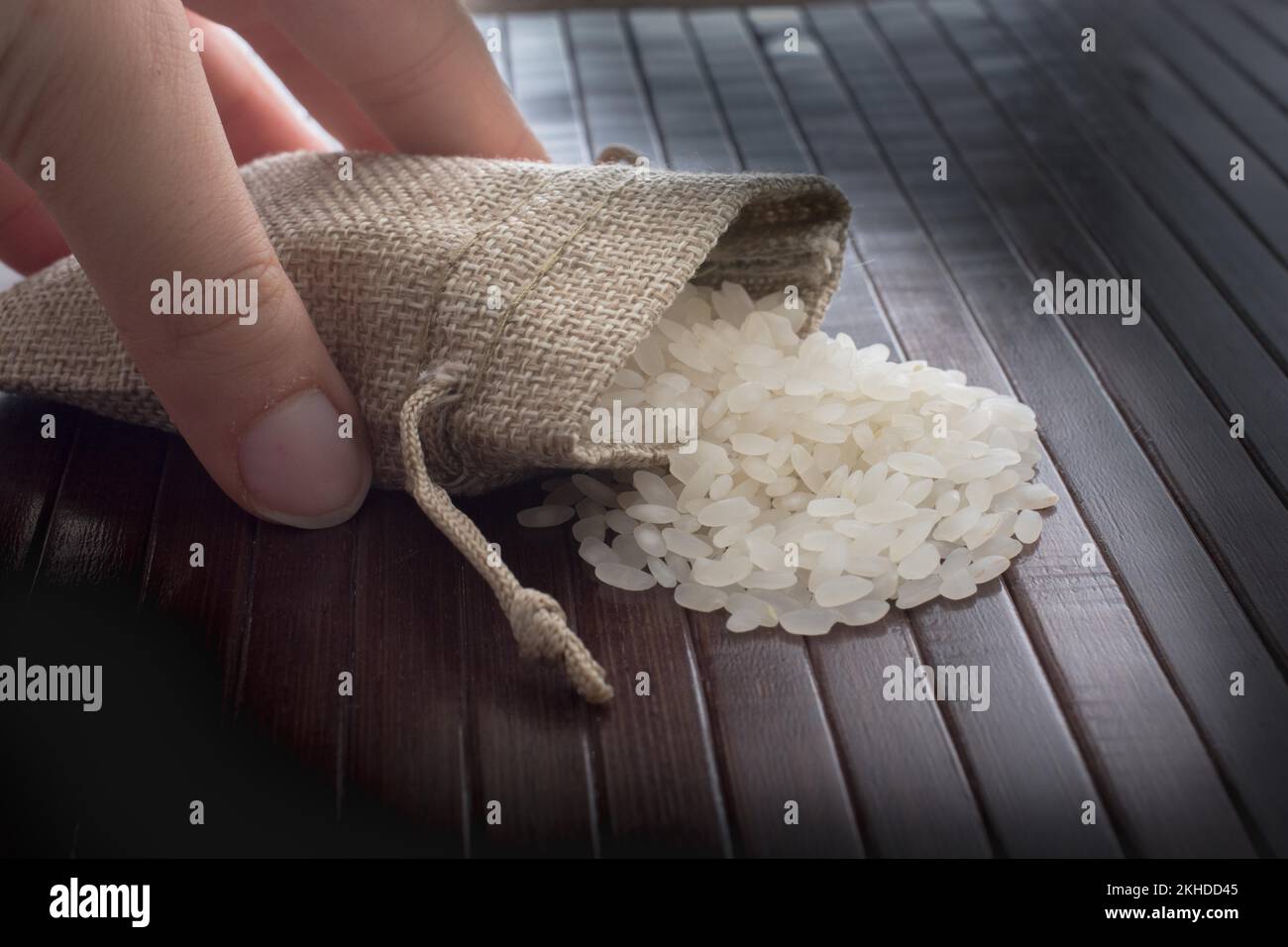 Mano che tiene la paglia sacchetto pieno di riso crudo su uno sfondo di legno Foto Stock