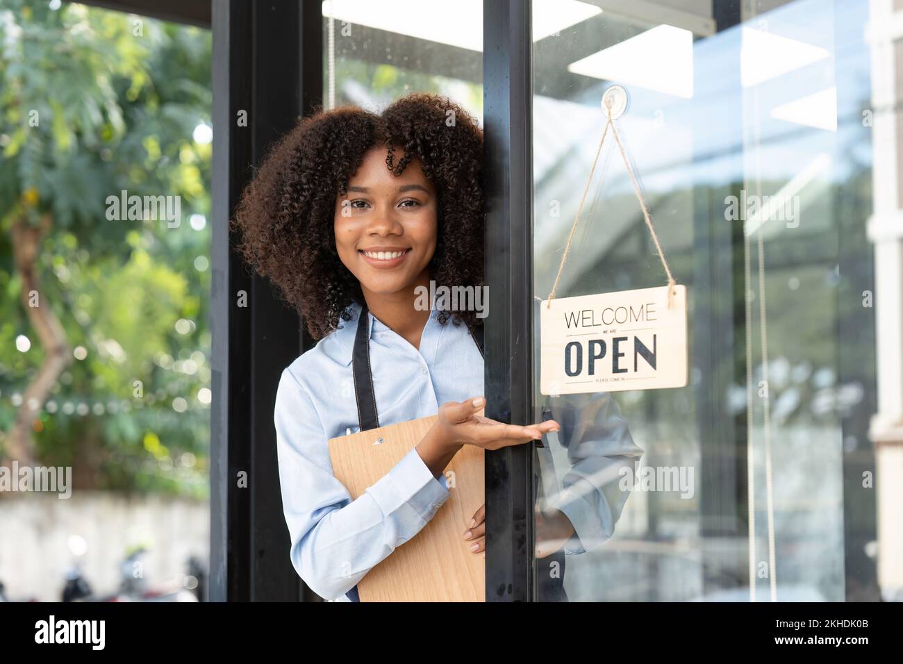 Piccola impresa africana donna proprietario sorridente mentre girando segno per l'apertura del caffè. Felice afro-americano cameriera imprenditore in grembiule presente segno su Foto Stock