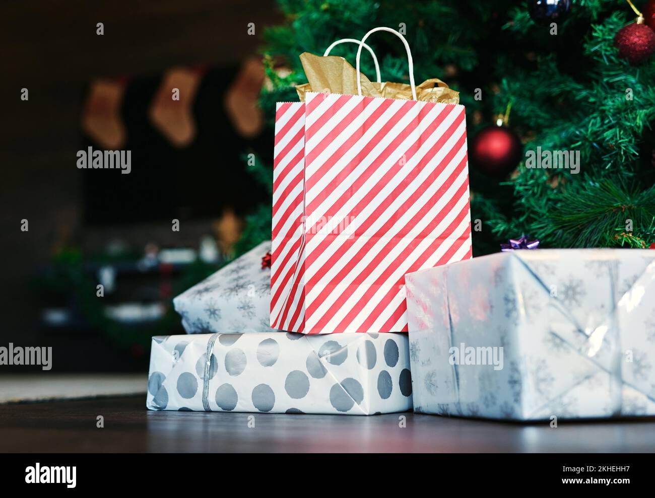 Natale, regalo e albero sul pavimento in casa per la sorpresa, la donazione e la celebrazione in stagione di festa. Borsa, scatola e presente sul pavimento da albero di natale Foto Stock