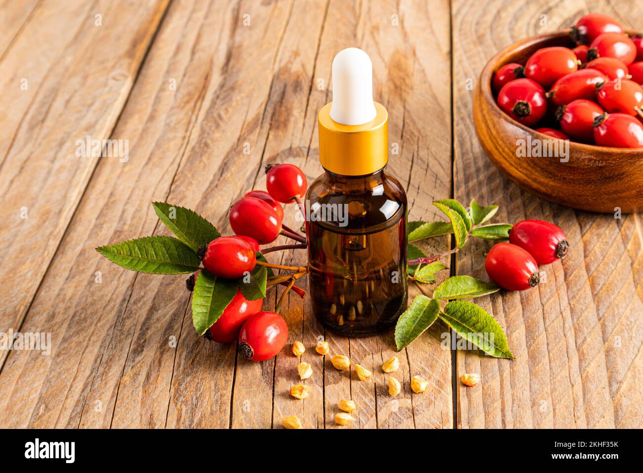 olio di rosa canina in una bottiglia cosmetica di vetro su fondo legno e una ciotola di frutta matura. il concetto di combattere l'invecchiamento della pelle. prevenzione delle rughe Foto Stock