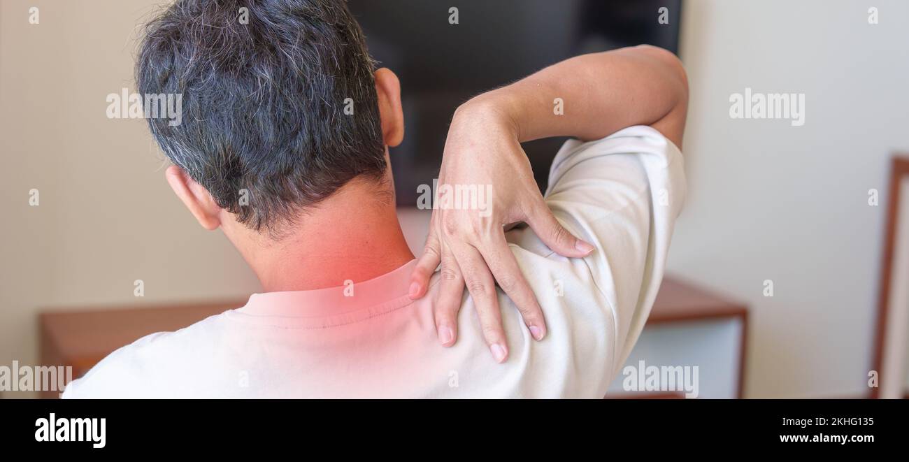 Uomo che ha dolore al collo e alle spalle durante la seduta sul divano. A causa di fibromialgia, reumatismi, dolore Scapolare, sindrome da ufficio e concetto ergonomico Foto Stock