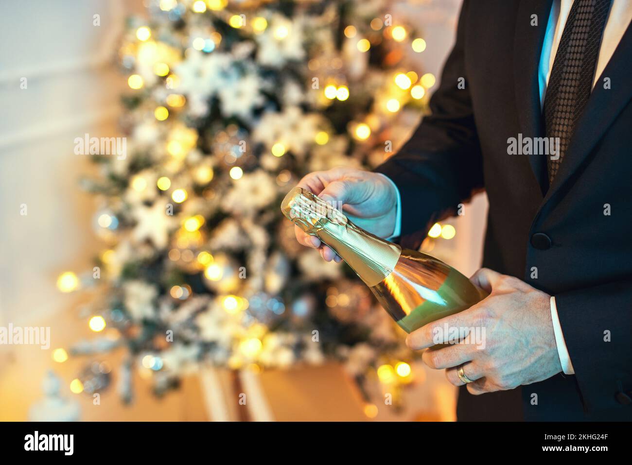 Primo piano scatto di un uomo in tuta aprire una bottiglia di champagne, c'è un albero di natale sullo sfondo. Foto Stock