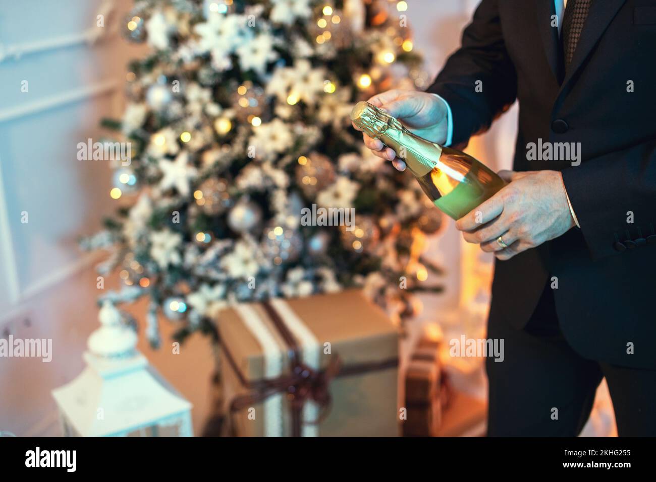 Primo piano scatto di un uomo in tuta aprire una bottiglia di champagne, c'è un albero di natale sullo sfondo. Foto Stock