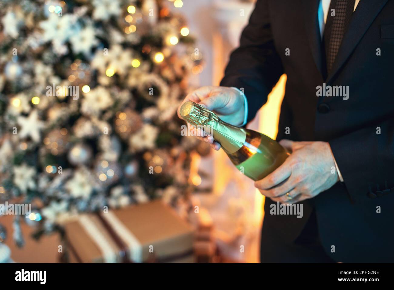 Primo piano scatto di un uomo in tuta aprire una bottiglia di champagne, c'è un albero di natale sullo sfondo. Foto Stock