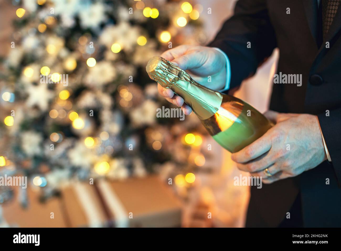 Primo piano scatto di un uomo in tuta aprire una bottiglia di champagne, c'è un albero di natale sullo sfondo. Foto Stock