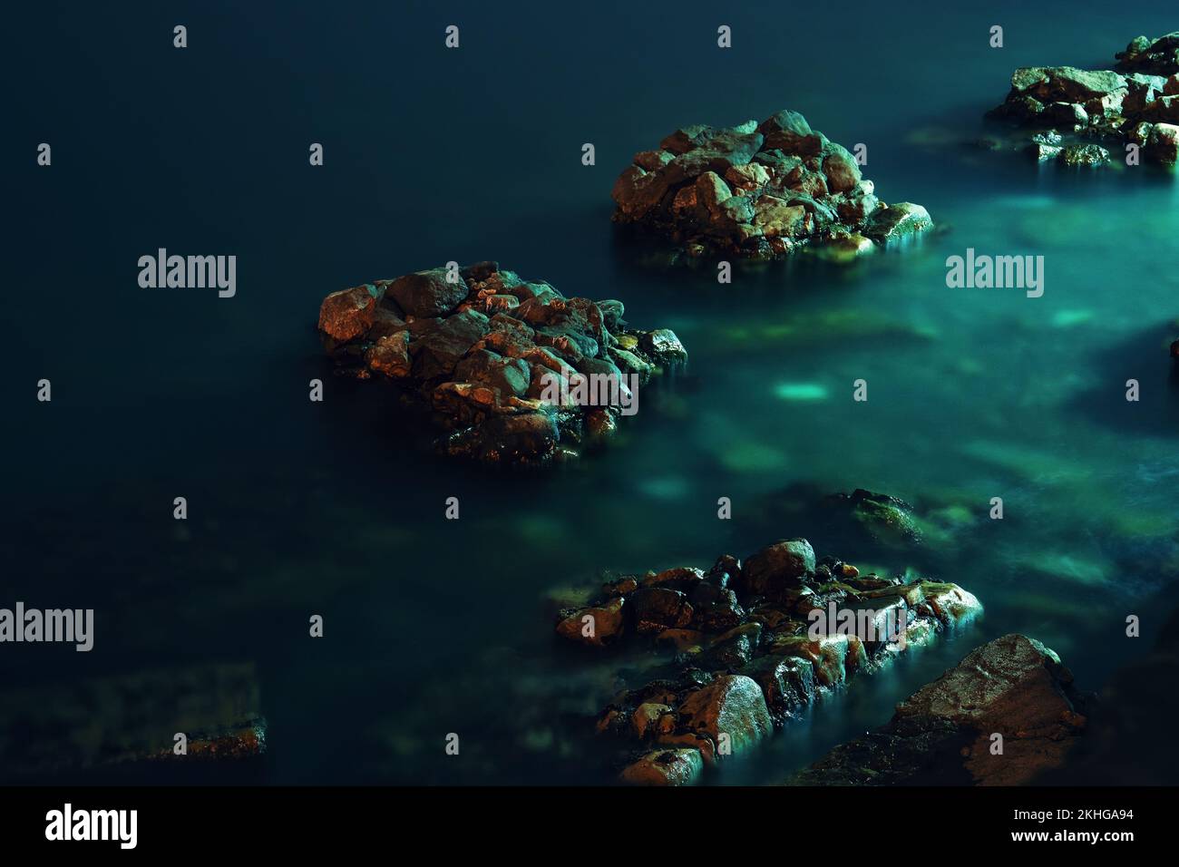 Pietre di roccia drammatiche scure nell'acqua verde blu del mare durante l'esposizione lunga di notte. Foto Stock