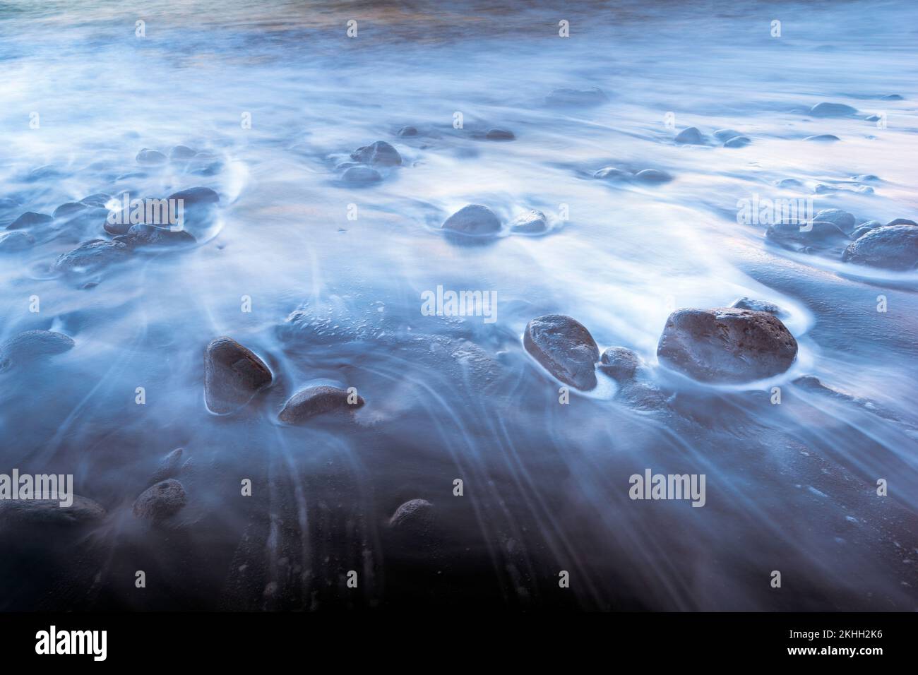 foto a lunga esposizione di onde di mare surf che scorrono tra grandi ciottoli Foto Stock