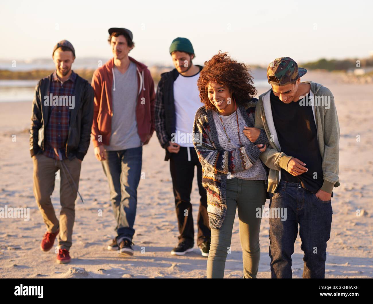 Vita una spiaggia, godere le onde. un gruppo di amici che cammina lungo una spiaggia al tramonto. Foto Stock