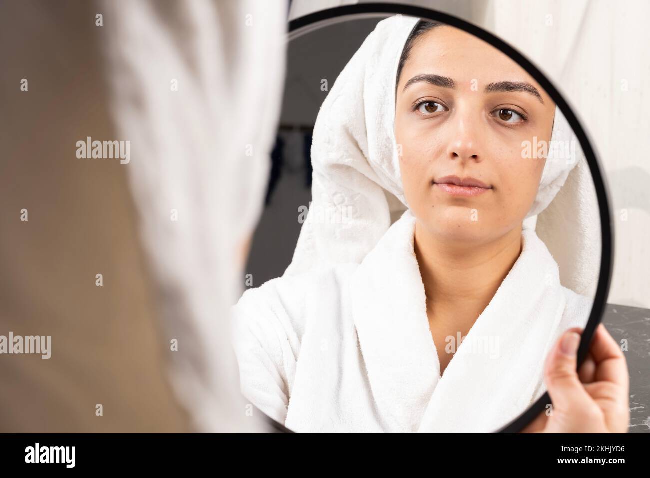 Bella donna che guarda specchio dopo doccia i suoi capelli avvolti in asciugamano. Idea di concetto di cura del mattino. Igiene personale, trattamenti cosmetici. Foto Stock