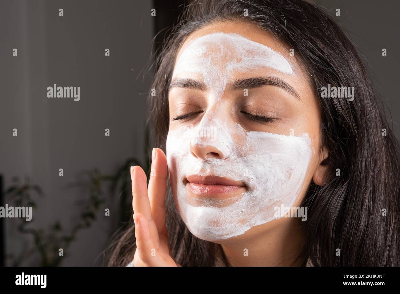 Applicazione maschera facciale, bella giovane donna caucasica a casa. Primo piano occhi chiusa ragazza con maschera di bellezza sul suo viso. Cura della pelle o trattamento di bellezza. Foto Stock