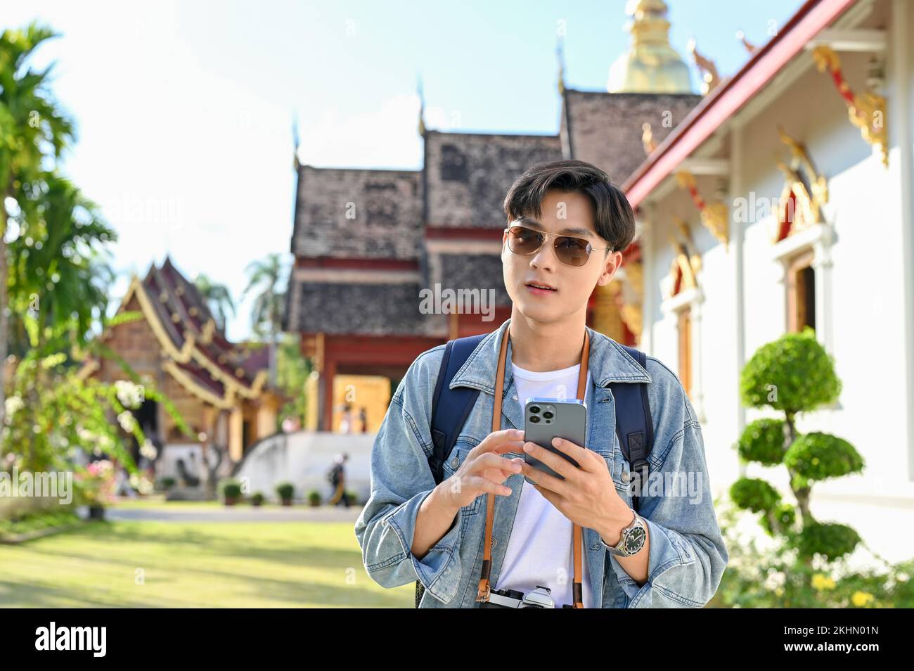 Bel giovane viaggiatore asiatico maschio utilizzando il suo smartphone, utilizzando l'applicazione mappa mentre passeggiando nel tempio tailandese. Concetto di viaggio in Asia Foto Stock