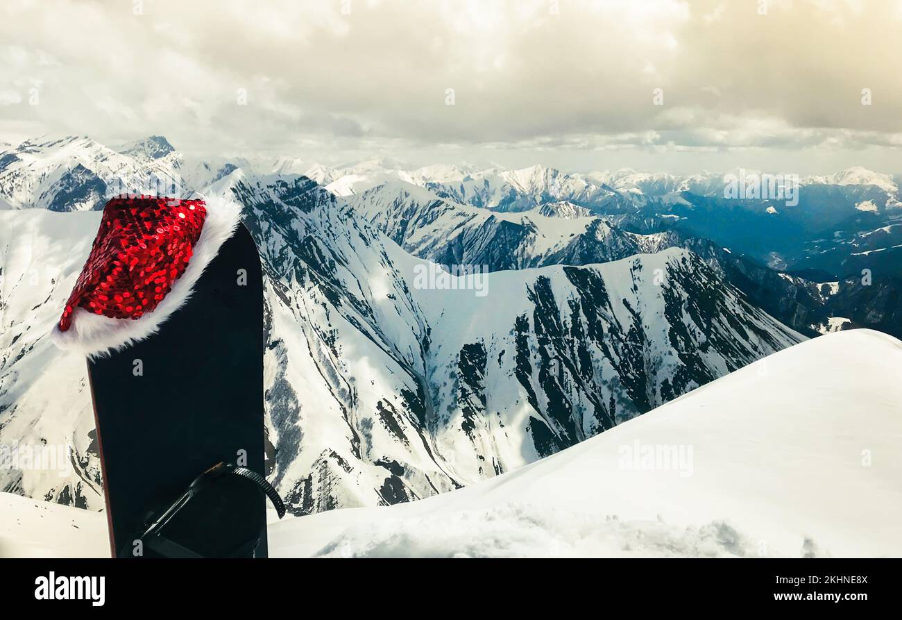 Snowboard nero con cappello di natale stand in neve belle montagne bianche del caucaso in Gudauri stazione sciistica punto panoramico in inverno. Stazione sciistica della Georgia Foto Stock