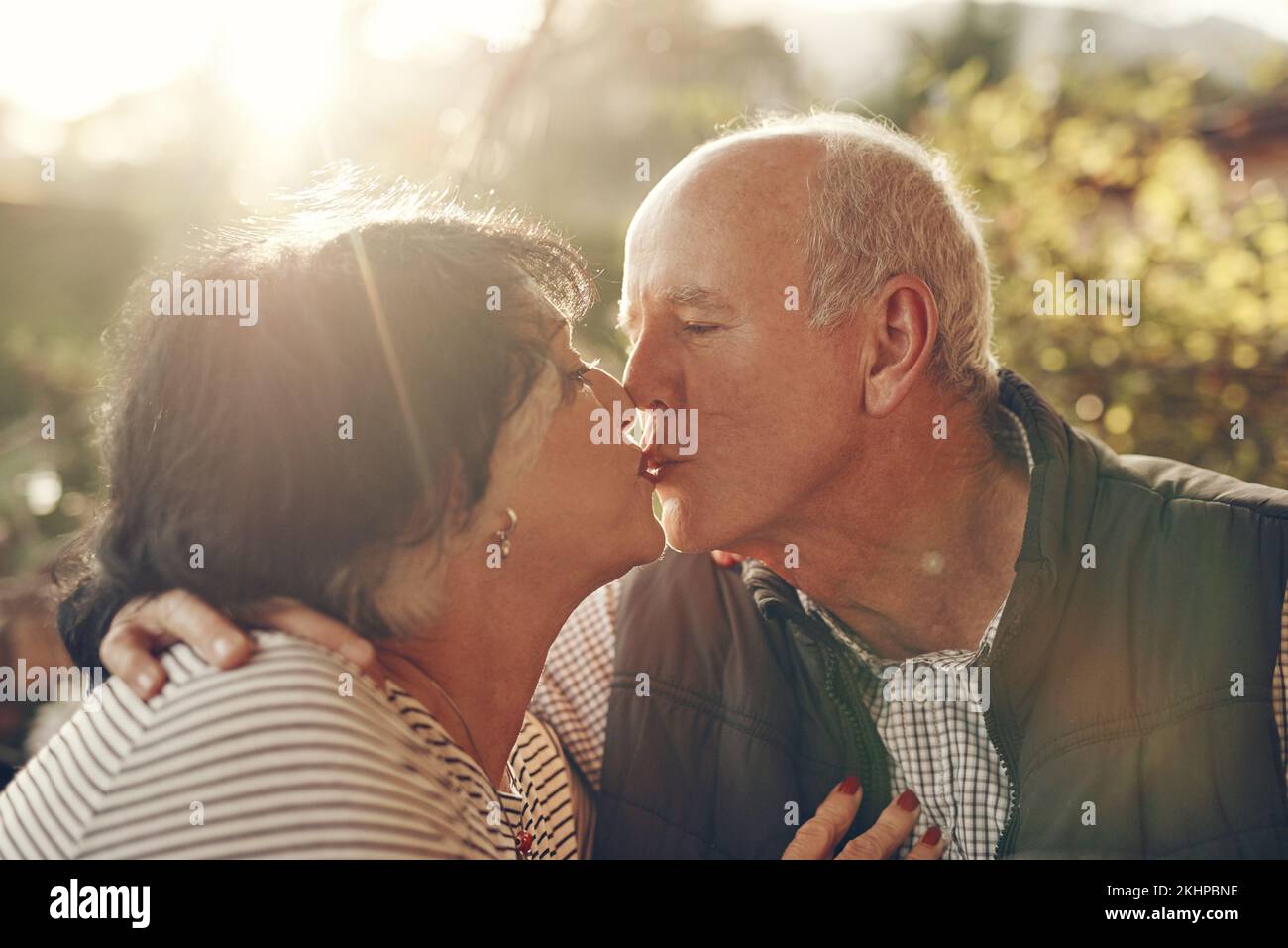 Bacio, amore e coppia anziana in natura, parco o all'aperto per il benessere pensione, la cura e la vita insieme nel sole estivo. Vacanze, viaggi e. Foto Stock