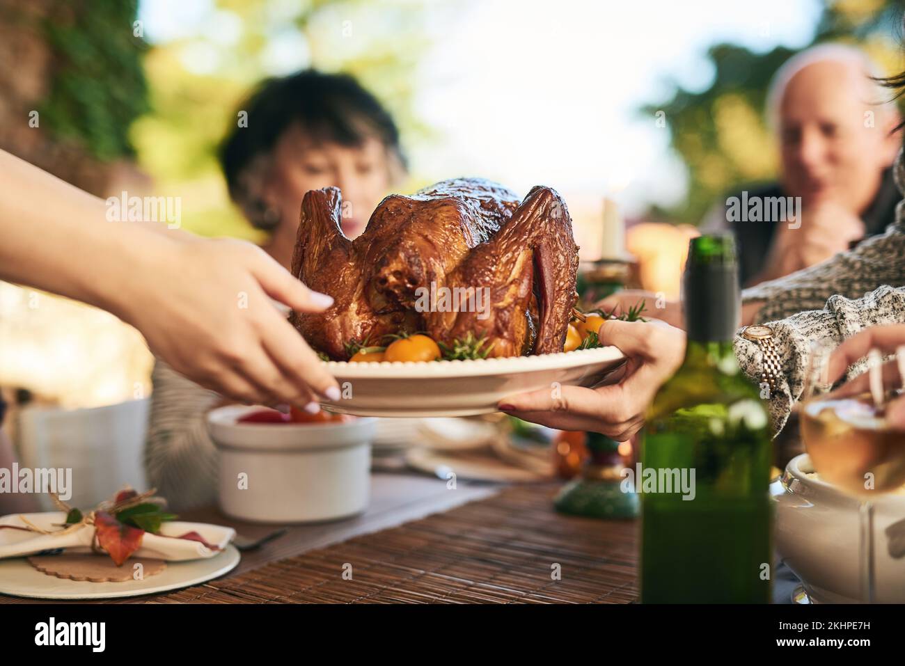 Ringraziamento, tacchino e mani con una famiglia che mangia un pasto all'aperto insieme in celebrazione della tradizione. Natale, pollo e festa con un uomo e. Foto Stock