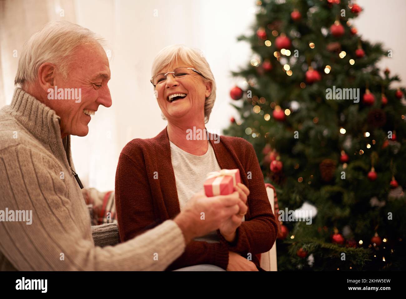 Felice, amore e coppia anziana con un dono per il Natale in celebrazione di una celebrazione spirituale a casa. Sorridi, sorpresa e la donna anziana ama dare Foto Stock