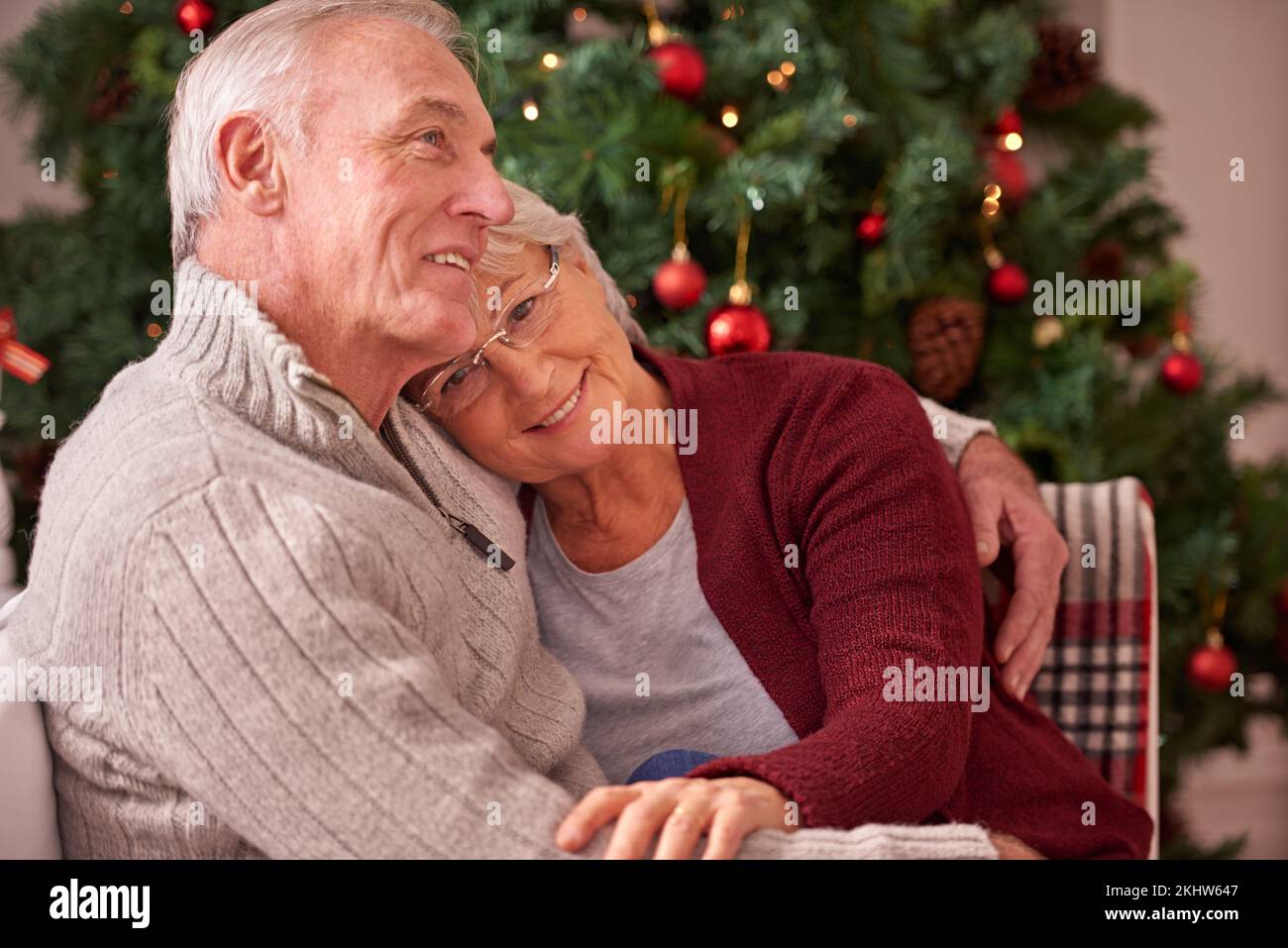 Natale, amore e coppia anziana abbracciare sul divano in casa, affetto e legame. Romanticismo, vacanze natalizie e felice anziano, donna in pensione e l'uomo abbracciano Foto Stock